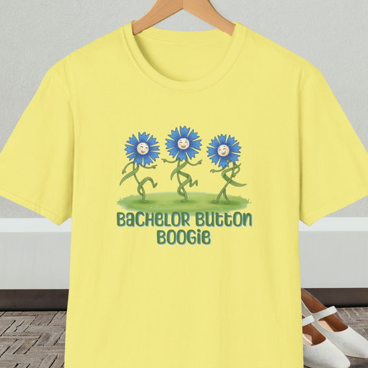 Yellow t-shirt with 'Bachelor Button Boogie' design featuring dancing blue flowers, on a hanger against a neutral background.