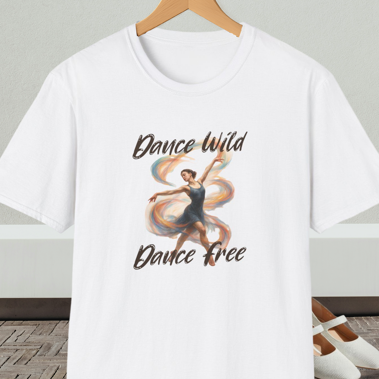 White t-shirt with a graphic of a dancer and text 'Dance Wild, Dance Free', on a hanger against a neutral background.