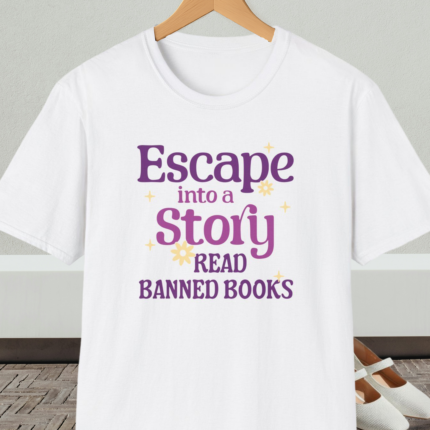 White t-shirt on a hanger, with text 'Escape into a Story, Read Banned Books'