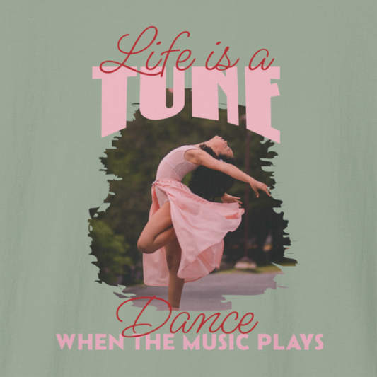 Close-up of a sage green T-shirt with a dancer in a pink dress and text 'Life is a tune, dance when the music plays'