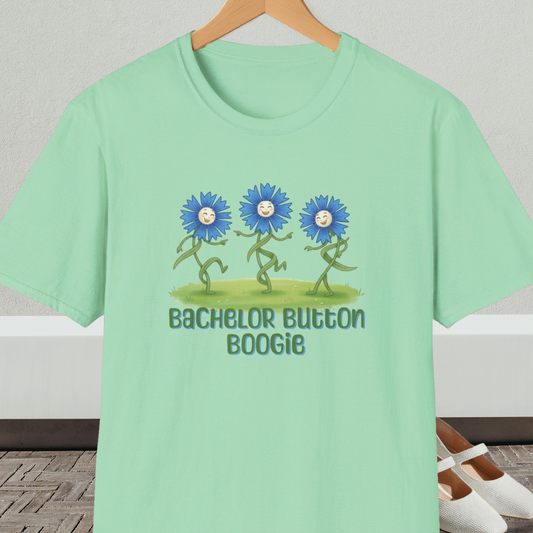 Light green t-shirt with 'Bachelor Button Boogie' design featuring dancing blue flowers, on a hanger against a neutral background.