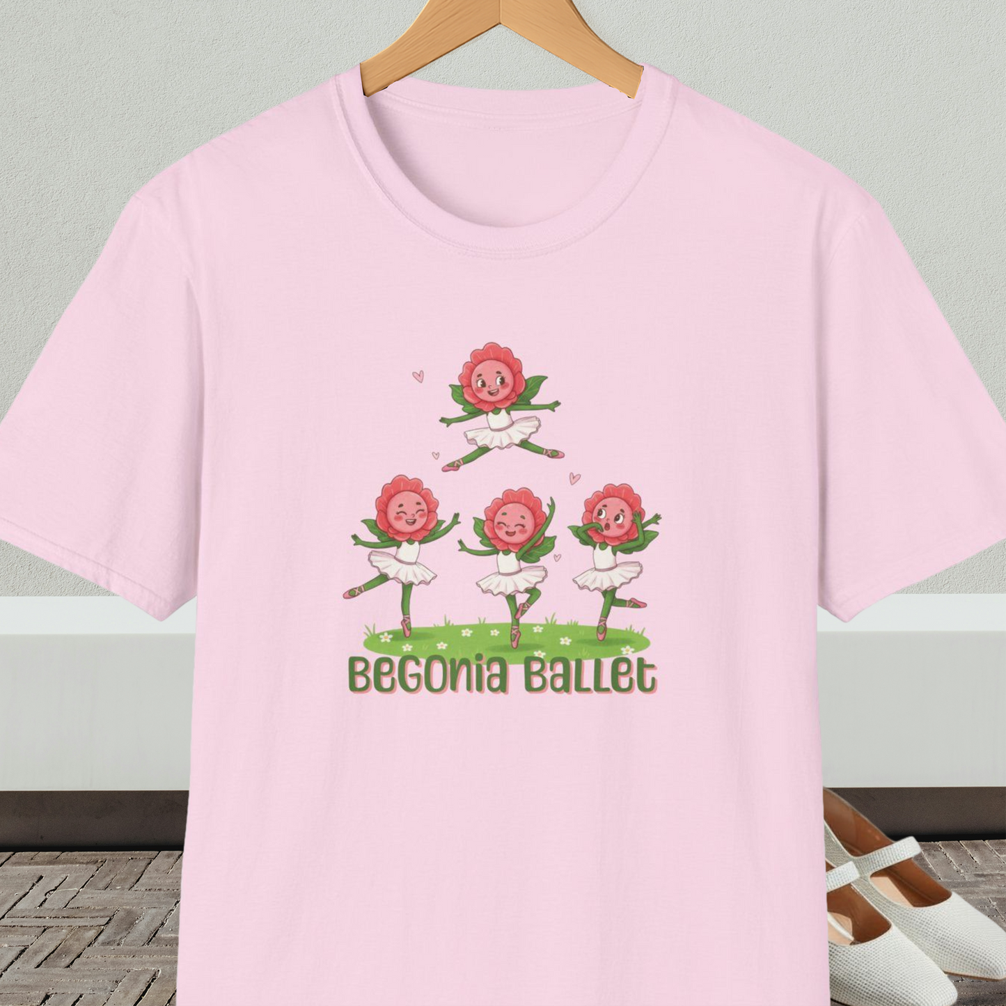 Light pink t-shirt with 'Begonia Ballet' design, on a hanger against a white wall.