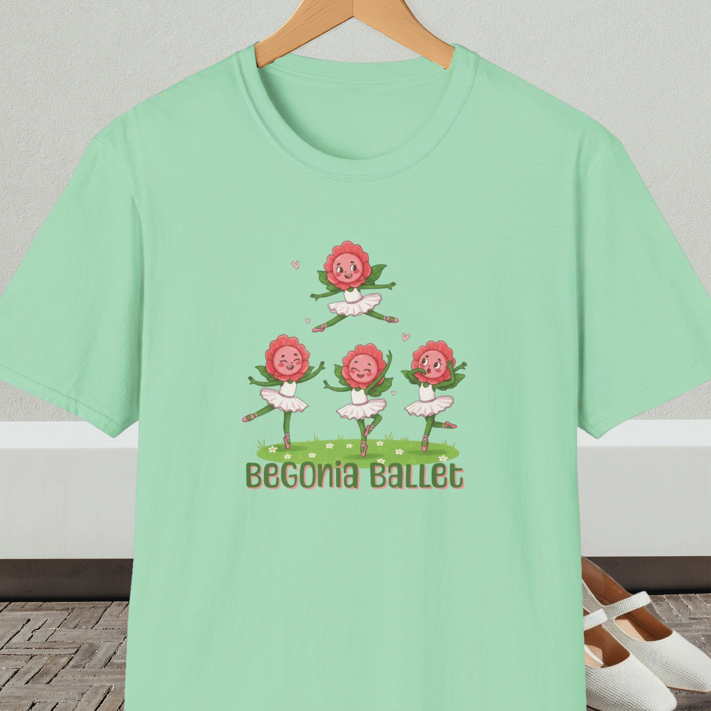 Light green t-shirt with 'Begonia Ballet' design, on a hanger against a white wall.