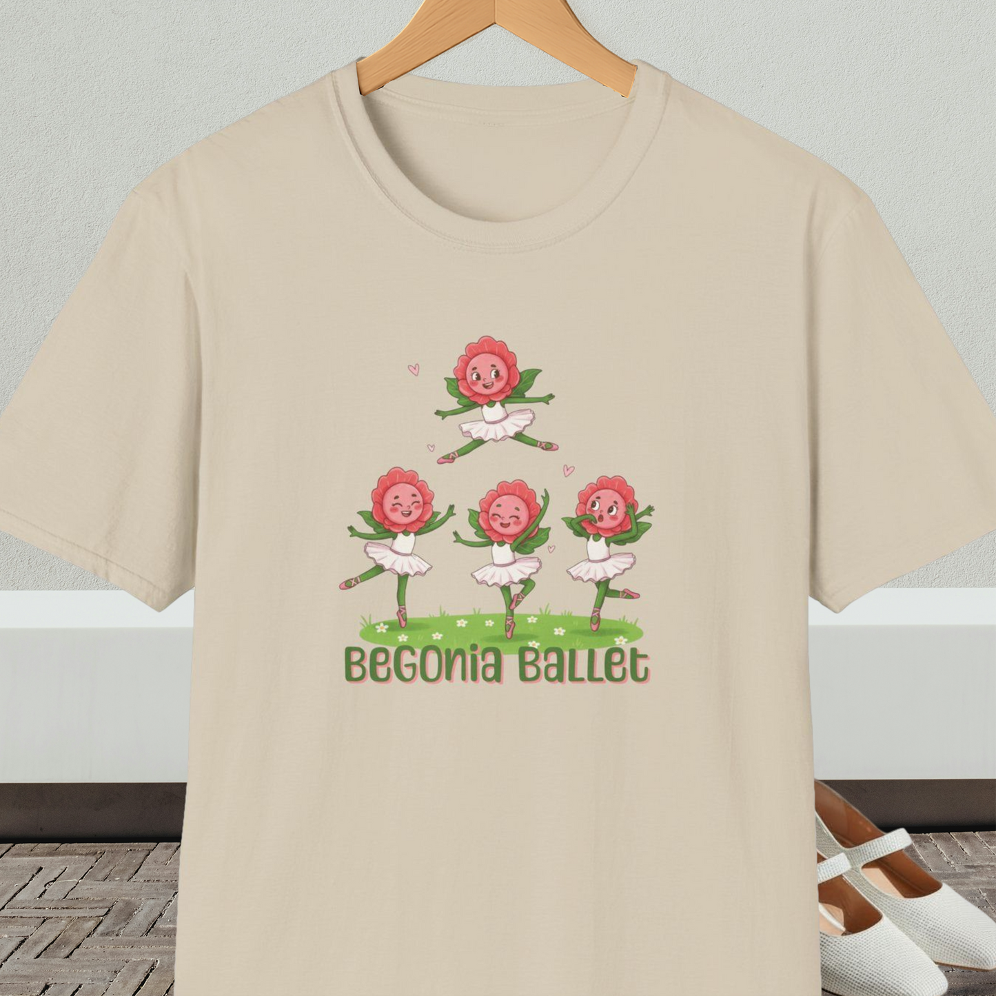 Beige t-shirt with 'Begonia Ballet' design, on a hanger against a white wall.