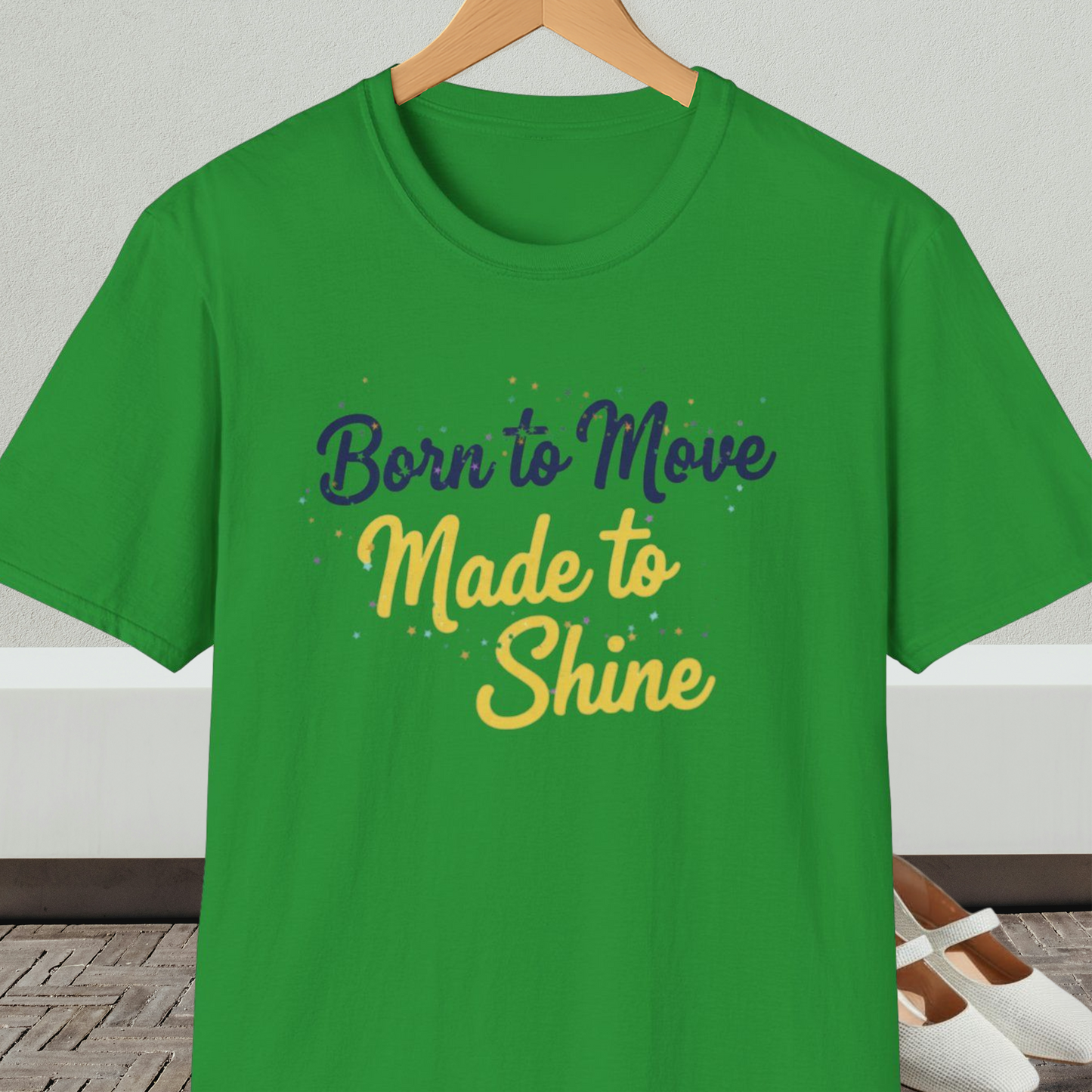Irish green t-shirt with 'Born to Move, Made to Shine' text, on a hanger against a white wall.