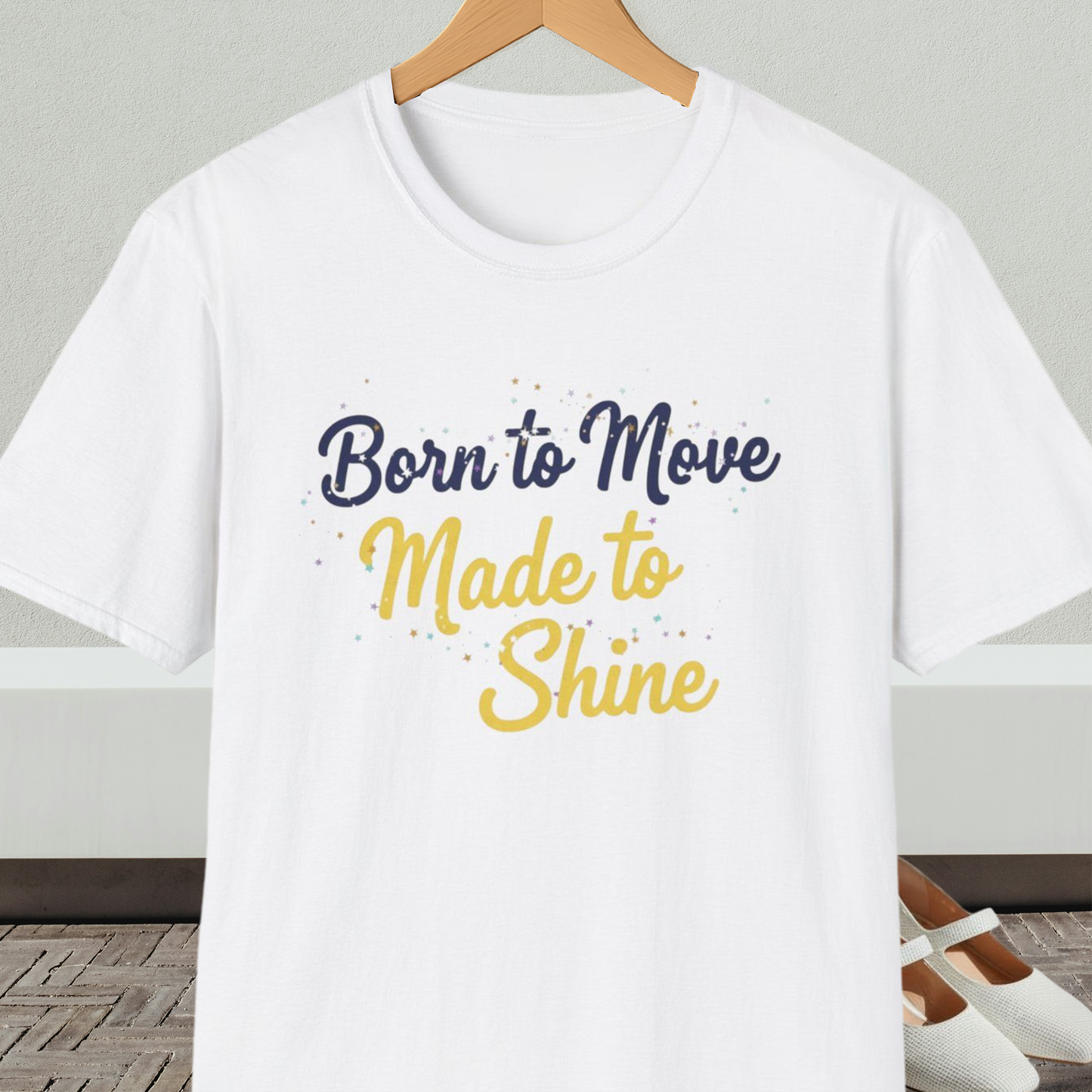 White t-shirt with 'Born to Move, Made to Shine' text, on a hanger against a neutral background.