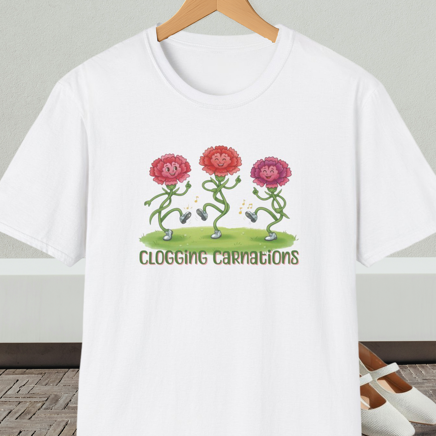 White t-shirt with dancing flower design and text 'Clogging Carnations', on a hanger in front of a neutral background.