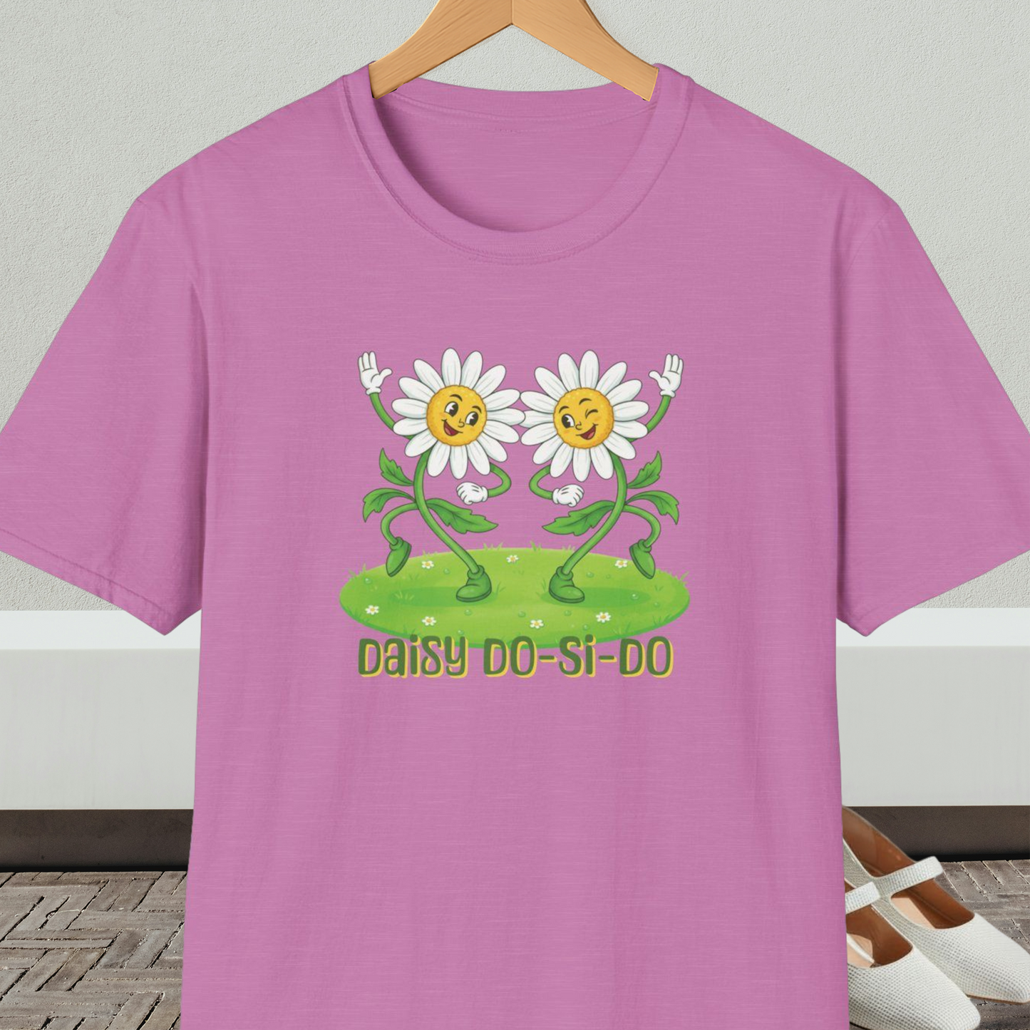 Orchid t-shirt with cartoon daisies and text 'Daisy Do-Si-Do' on a wooden hanger against a white wall.