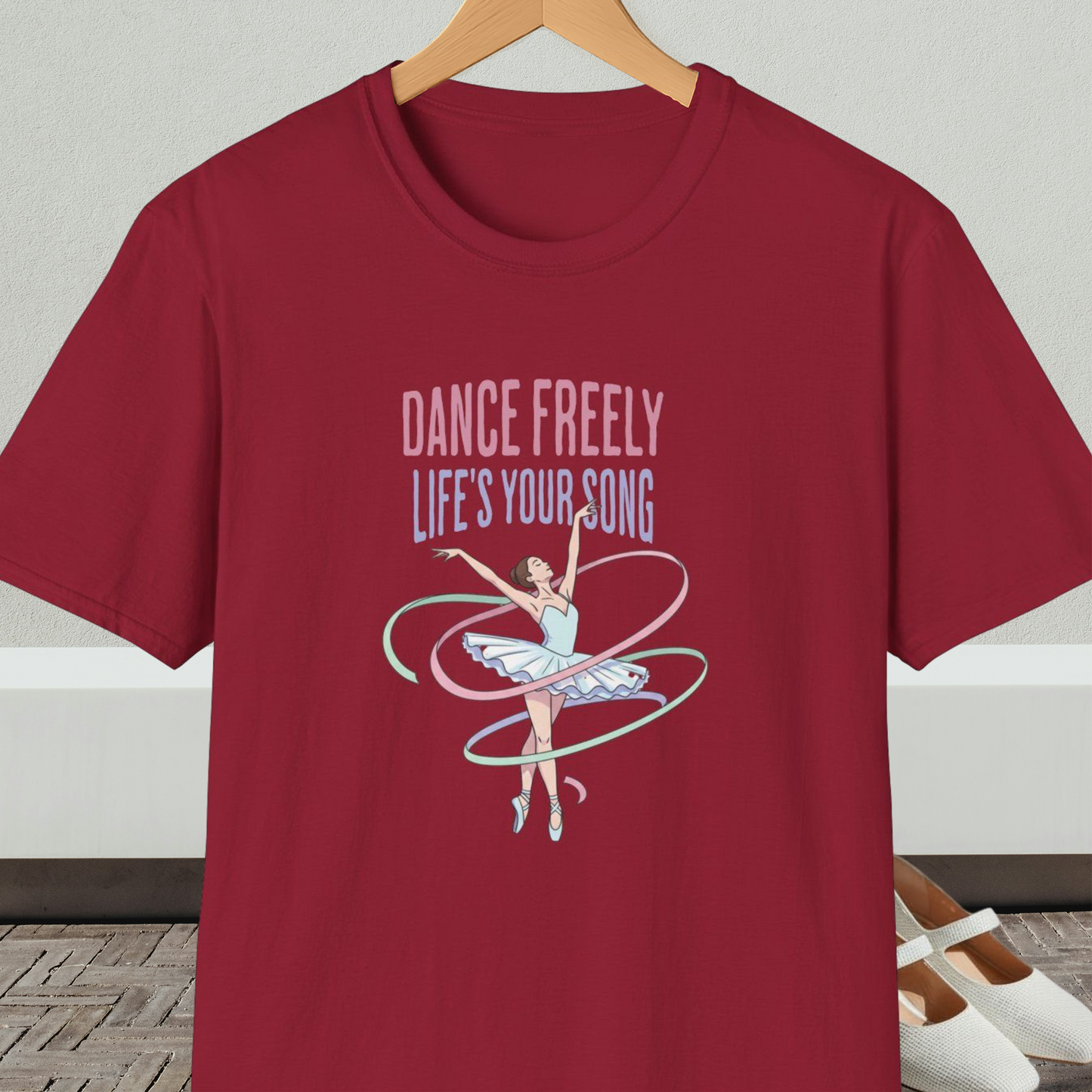 Dark red t-shirt with ballet design and text 'Dance Freely Life's Your Song', on a hanger against a neutral background