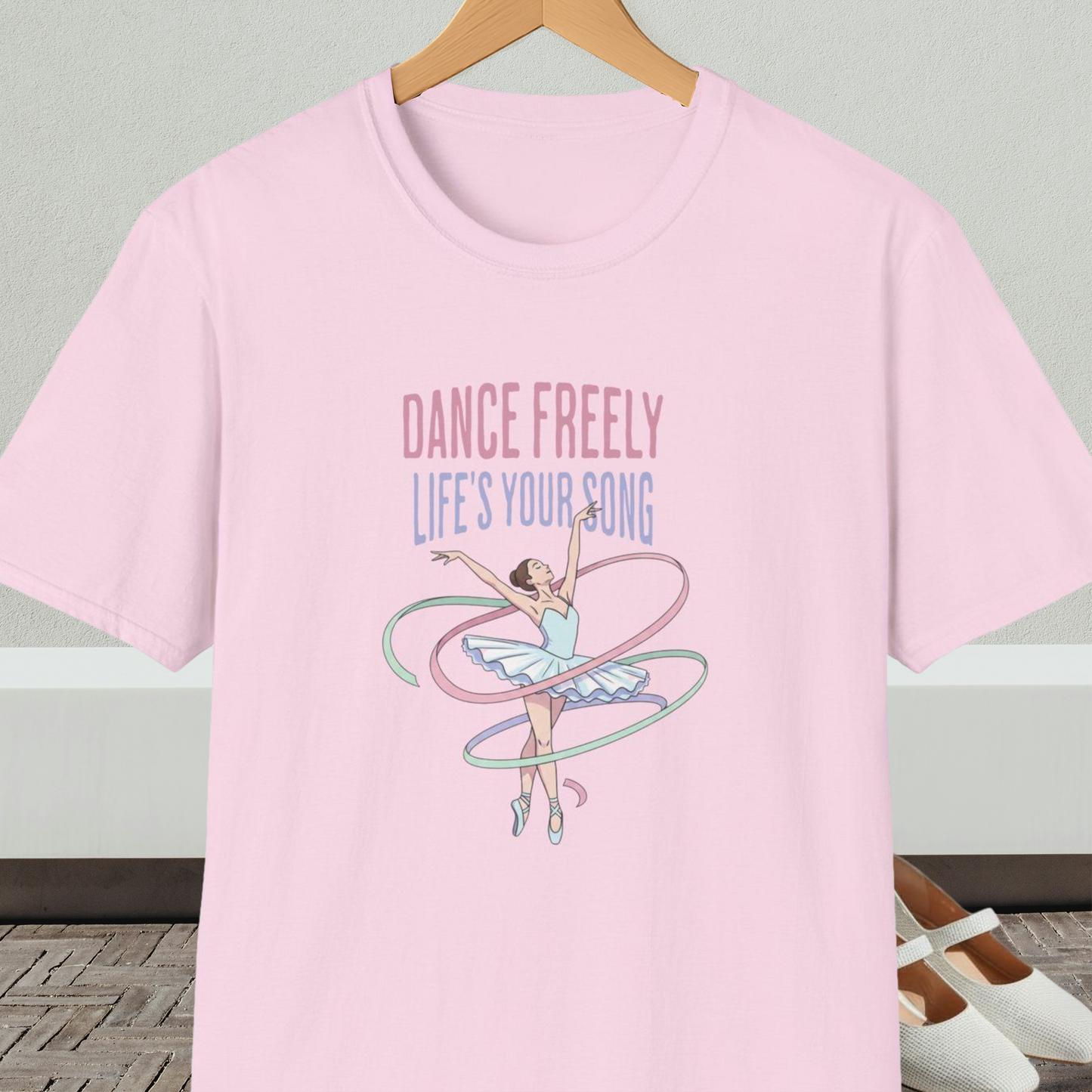 Light pink t-shirt with ballet design and text 'Dance Freely Life's Your Song', on a hanger against a neutral background