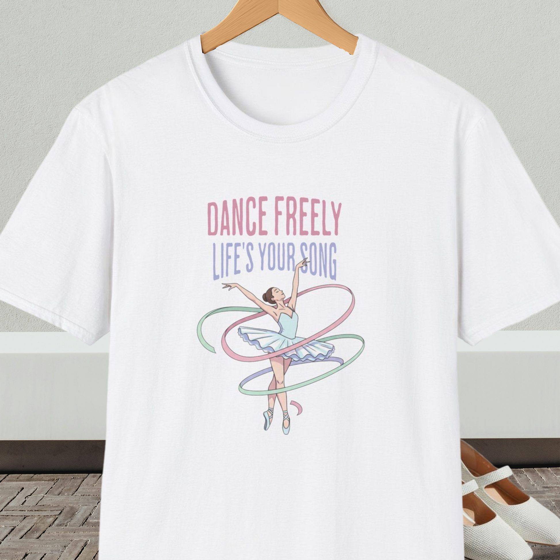 White t-shirt with ballet design and text 'Dance Freely Life's Your Song', on a hanger against a neutral background