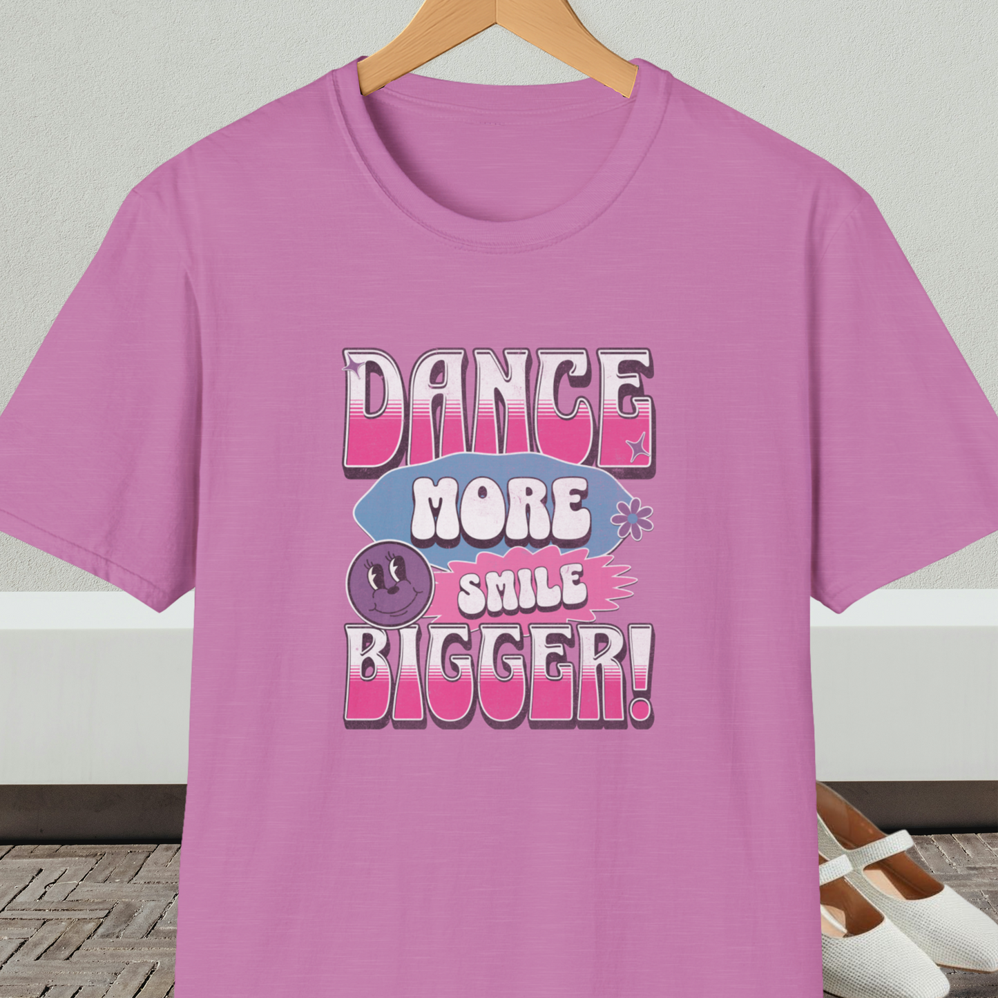Orchid t-shirt with 'Dance More Smile Bigger!' retro text, on a hanger against a neutral background.