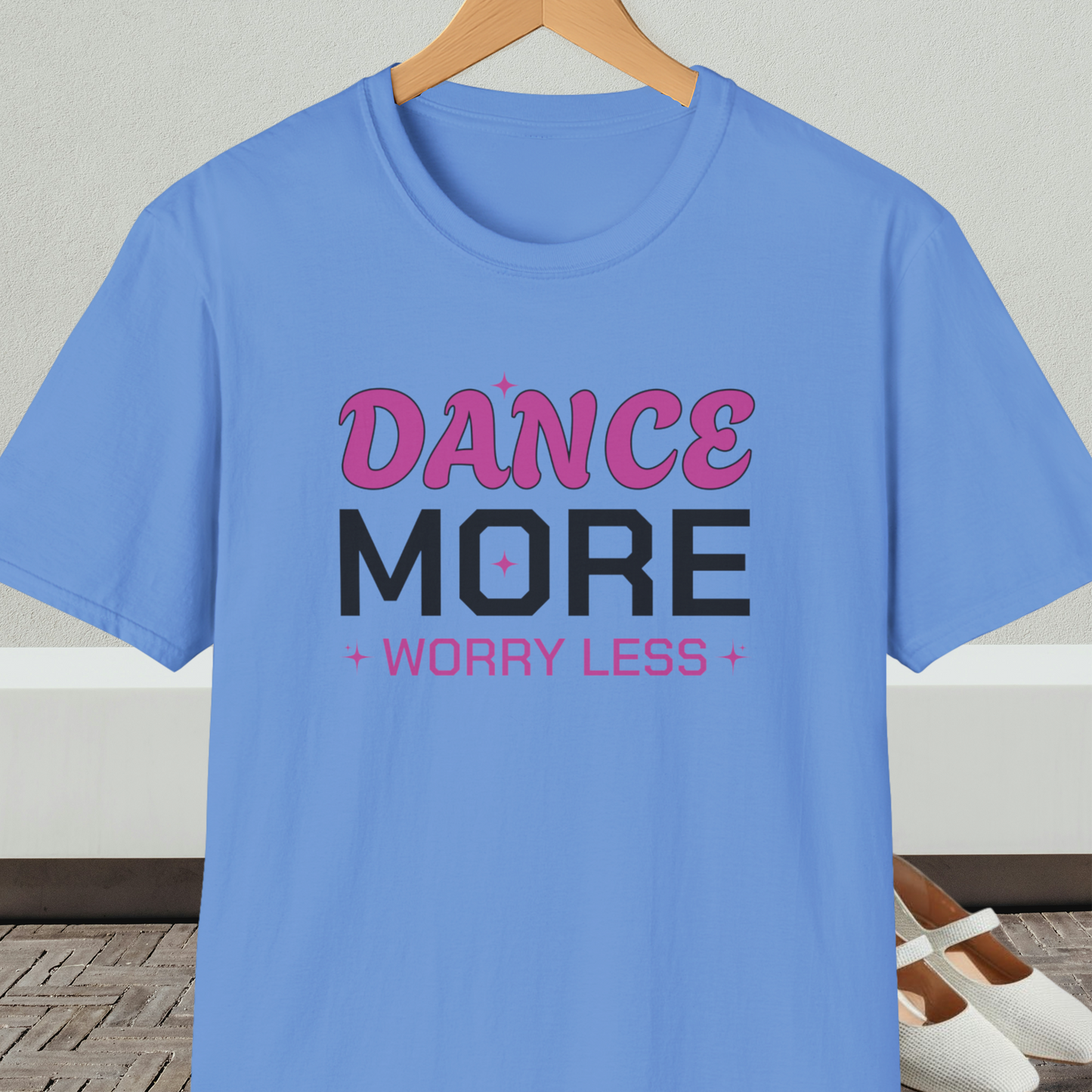 Blue t-shirt with 'Dance More Worry Less' text, on a hanger against a neutral background