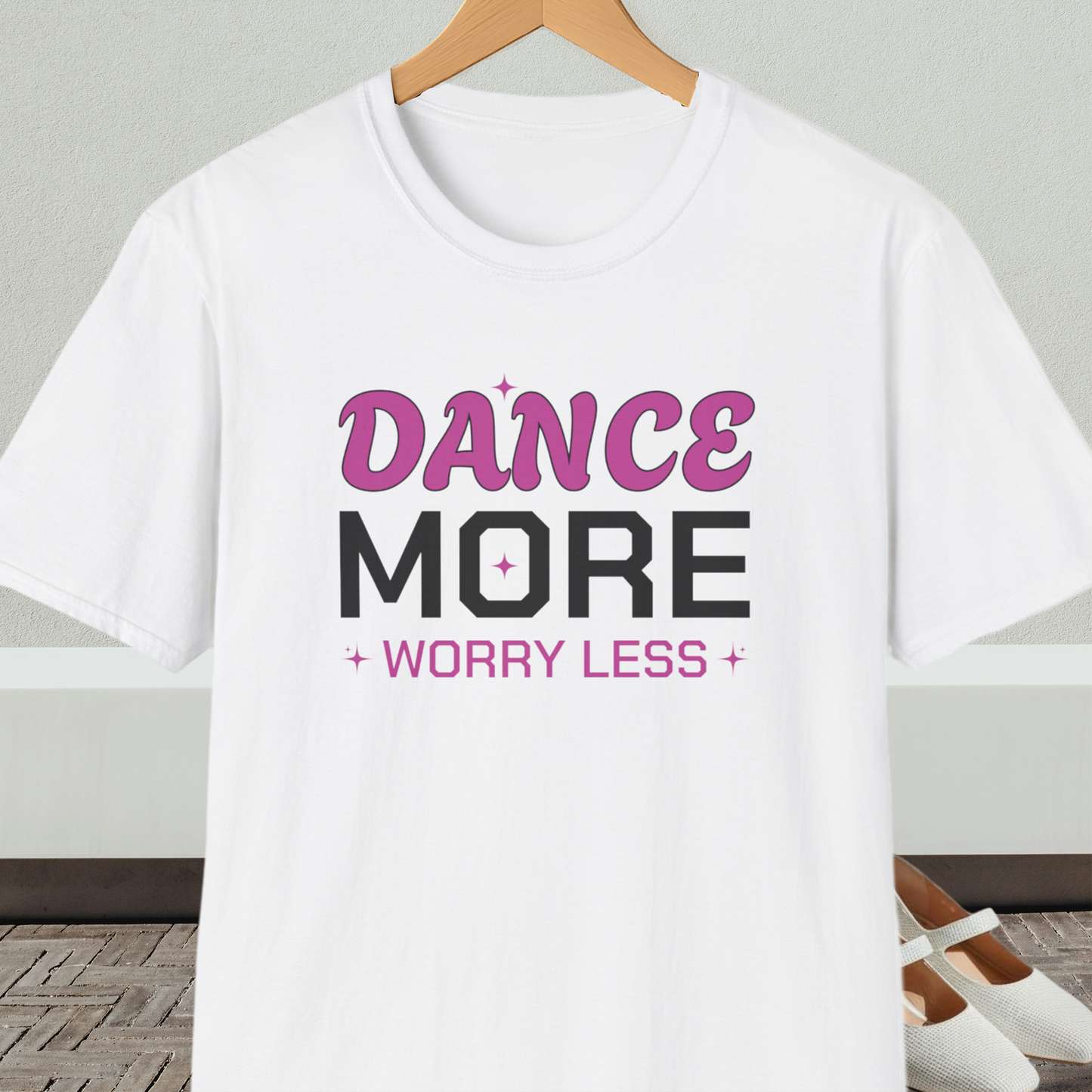 White t-shirt with 'Dance More Worry Less' text, on a hanger against a neutral background