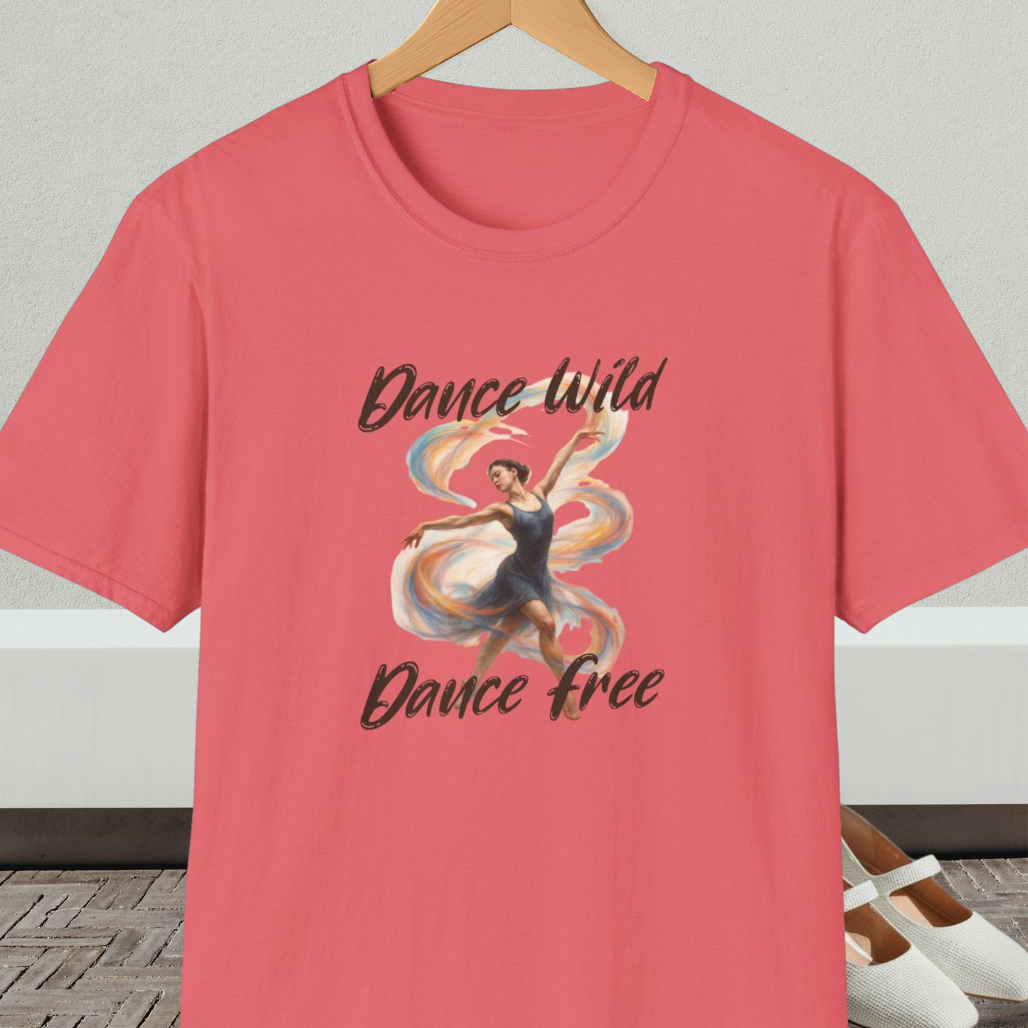 Coral t-shirt with a graphic of a dancer and text 'Dance Wild, Dance Free', on a hanger against a neutral background.