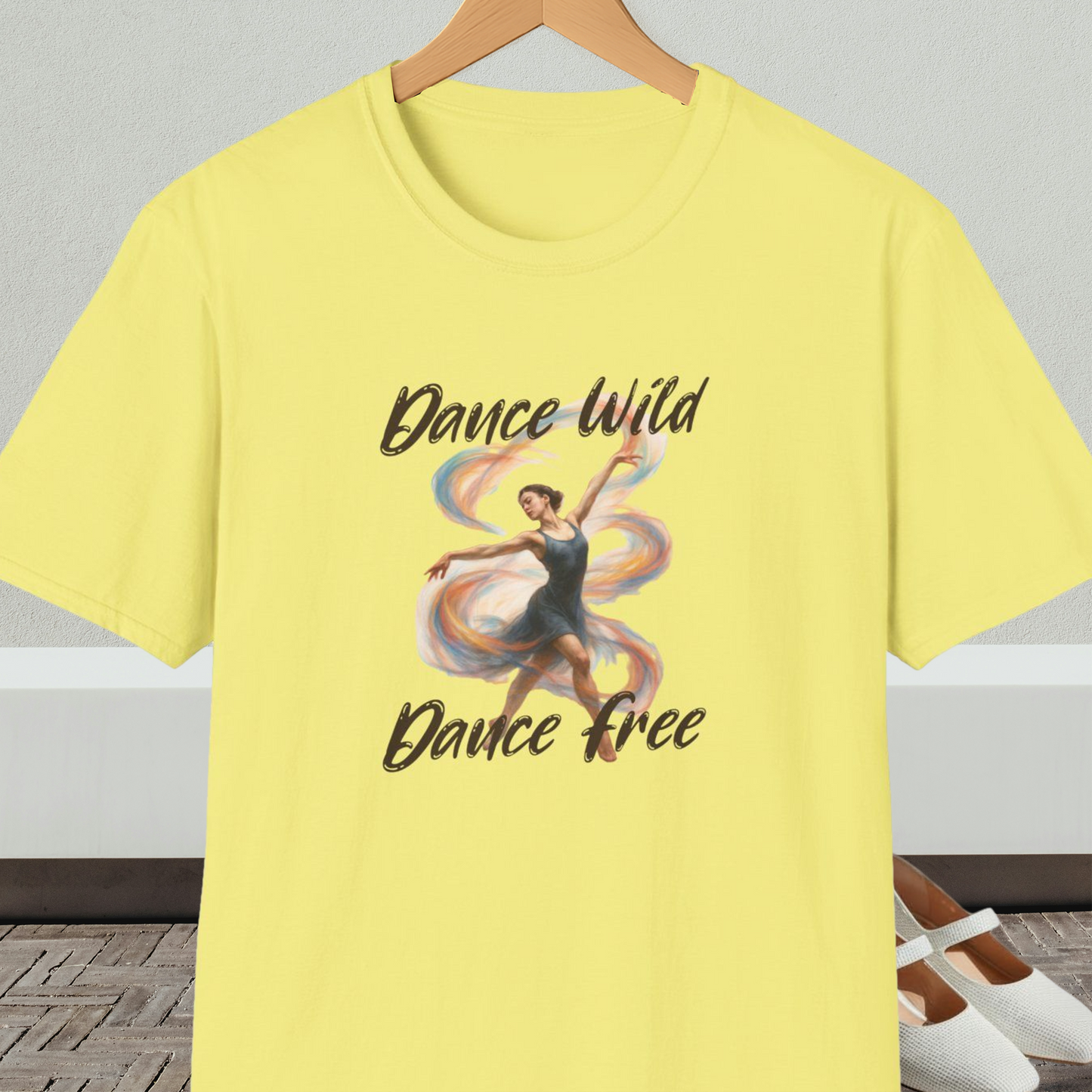 Yellow t-shirt with a graphic of a dancer and text 'Dance Wild, Dance Free', on a hanger against a neutral background.