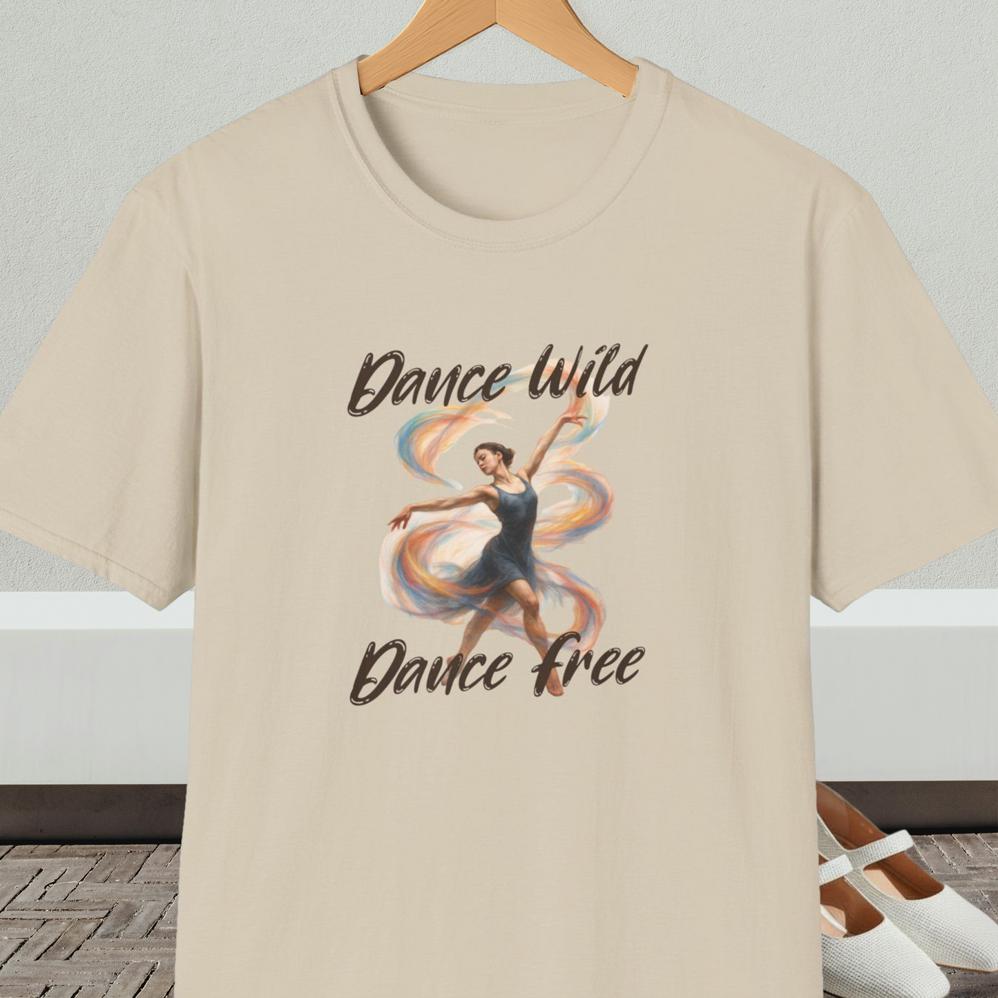 Beige t-shirt with a graphic of a dancer and text 'Dance Wild, Dance Free', on a hanger against a neutral background.
