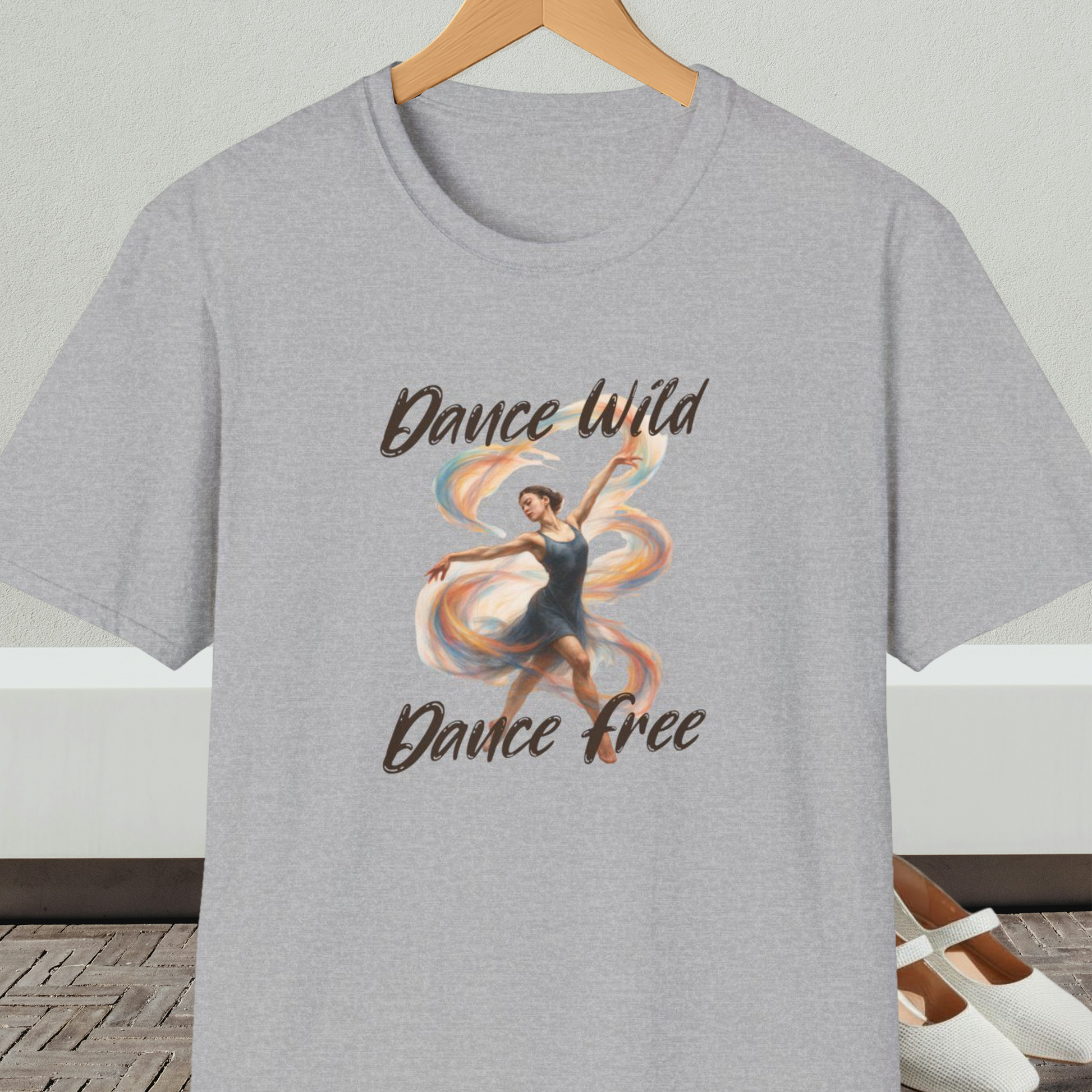 Gray t-shirt with a graphic of a dancer and text 'Dance Wild, Dance Free', on a hanger against a neutral background.