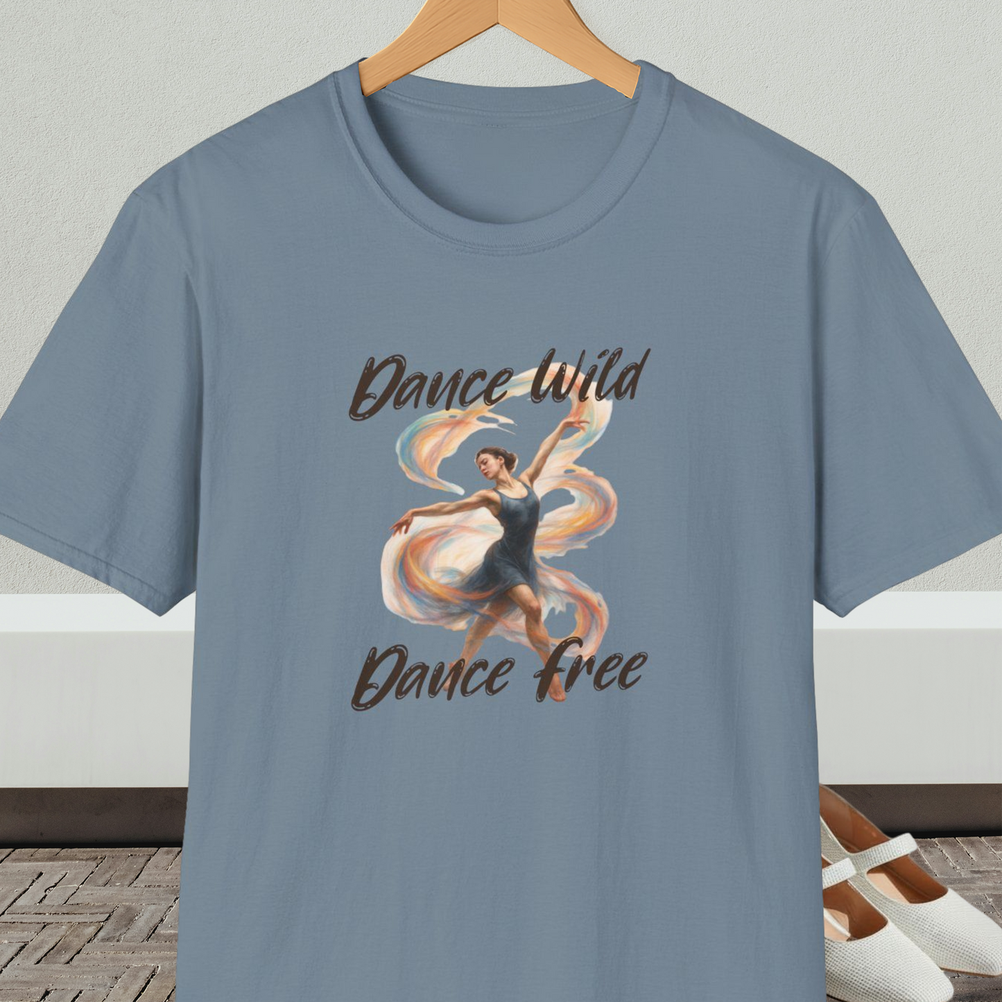 Stone blue t-shirt with a graphic of a dancer and text 'Dance Wild, Dance Free', on a hanger against a neutral background.