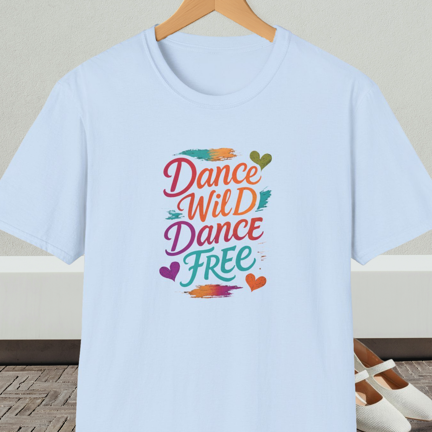 Light blue t-shirt with colorful 'Dance Wild Dance Free' text, on a hanger against a neutral background.