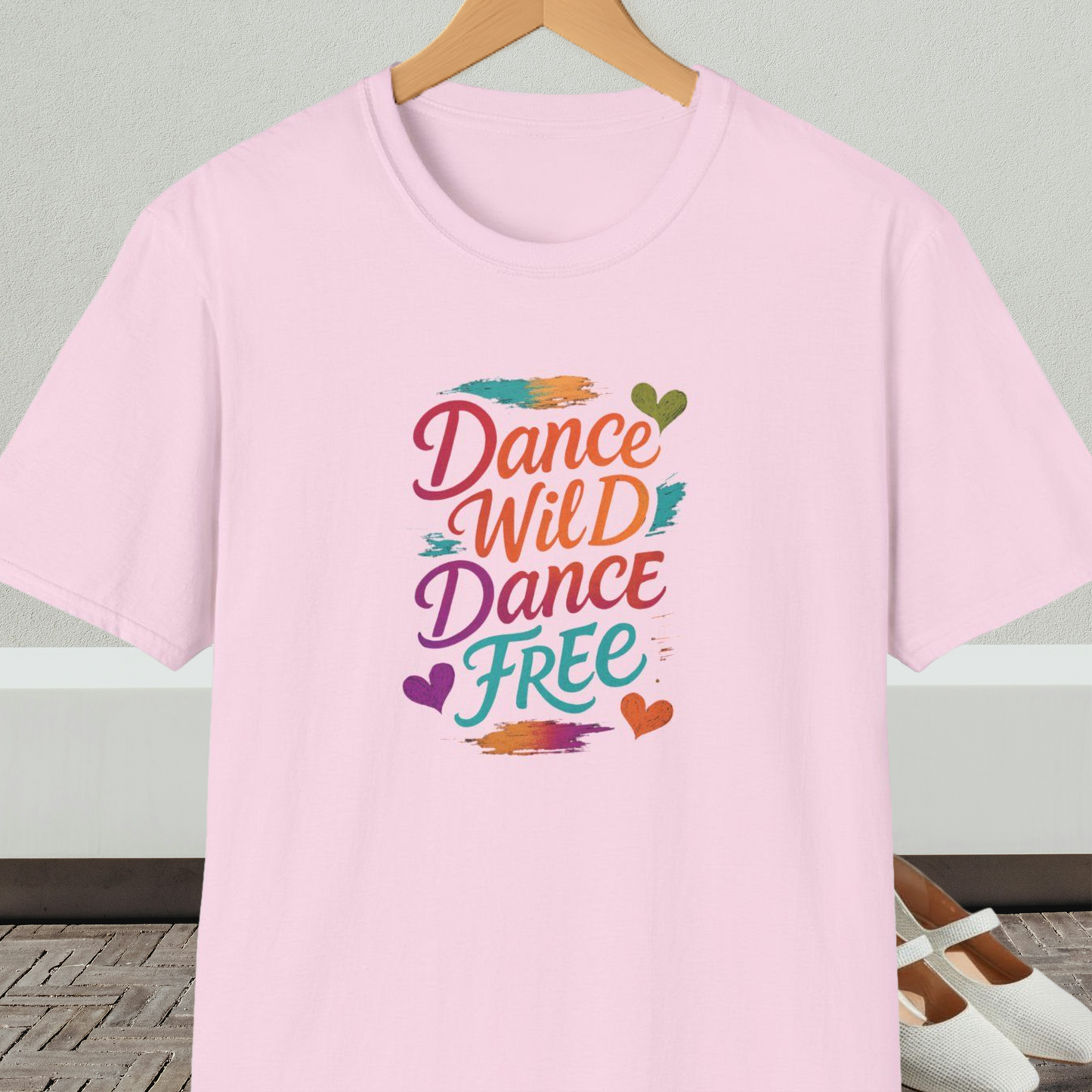 Light pink t-shirt with colorful 'Dance Wild Dance Free' text, on a hanger against a neutral background.