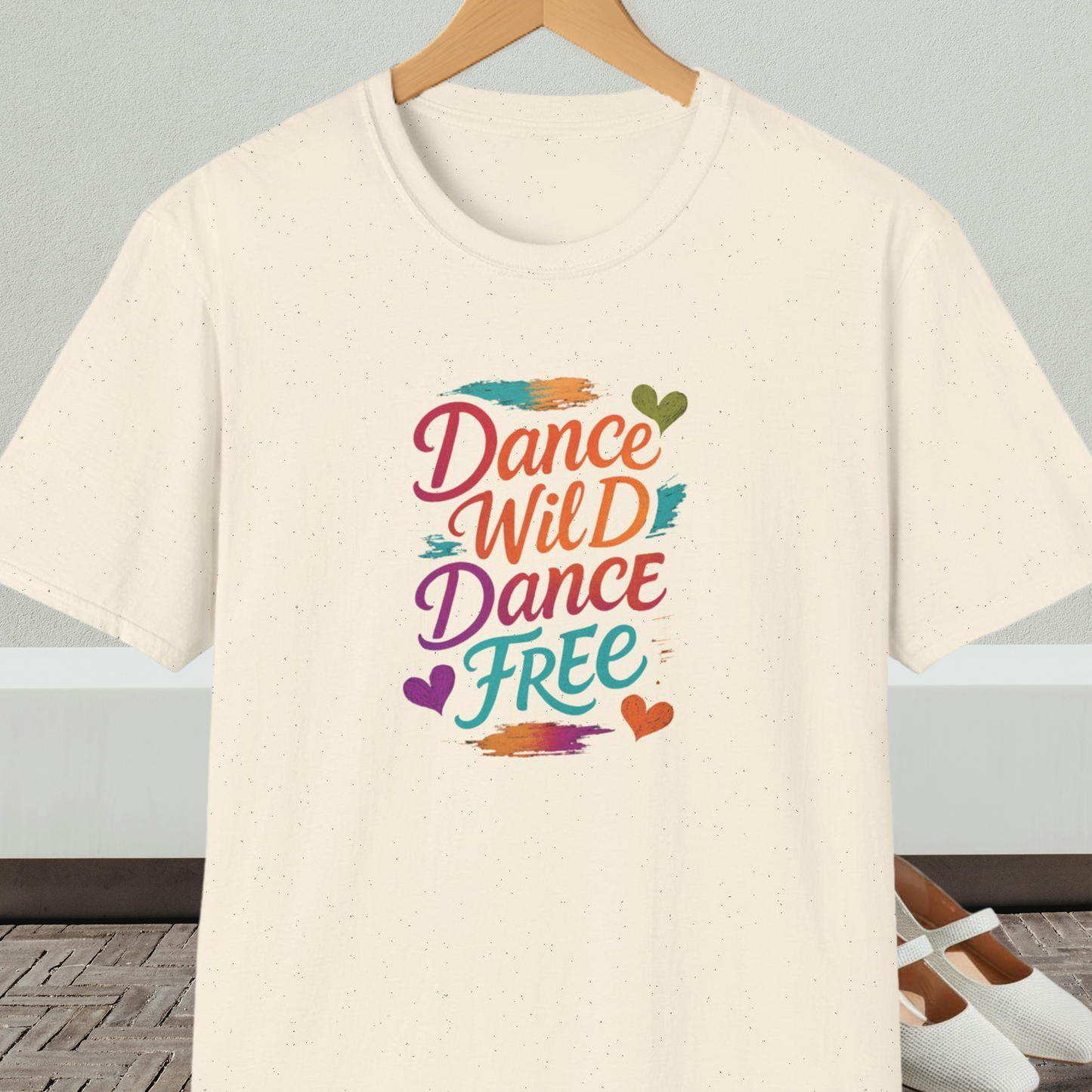 Natural beige t-shirt with colorful 'Dance Wild Dance Free' text, on a hanger against a neutral background.