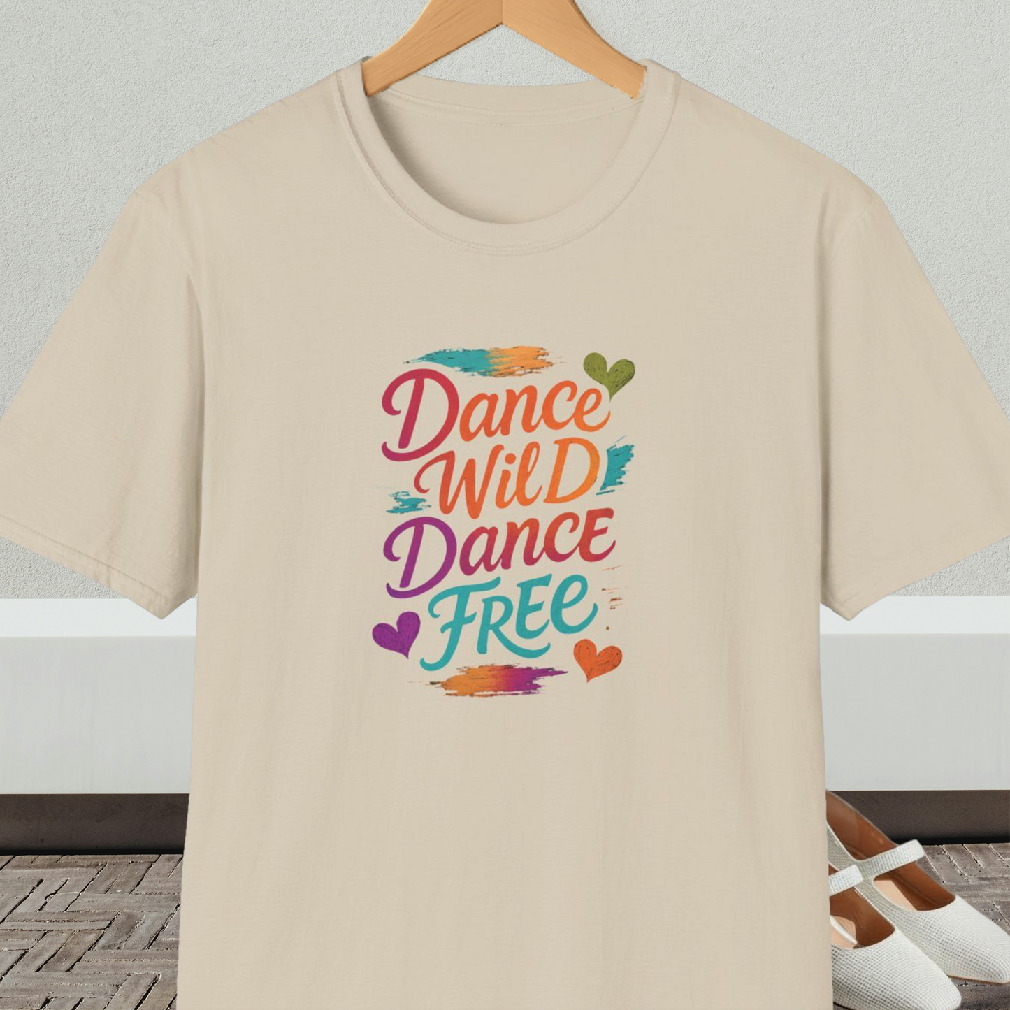 Beige t-shirt with colorful 'Dance Wild Dance Free' text, on a hanger against a neutral background.