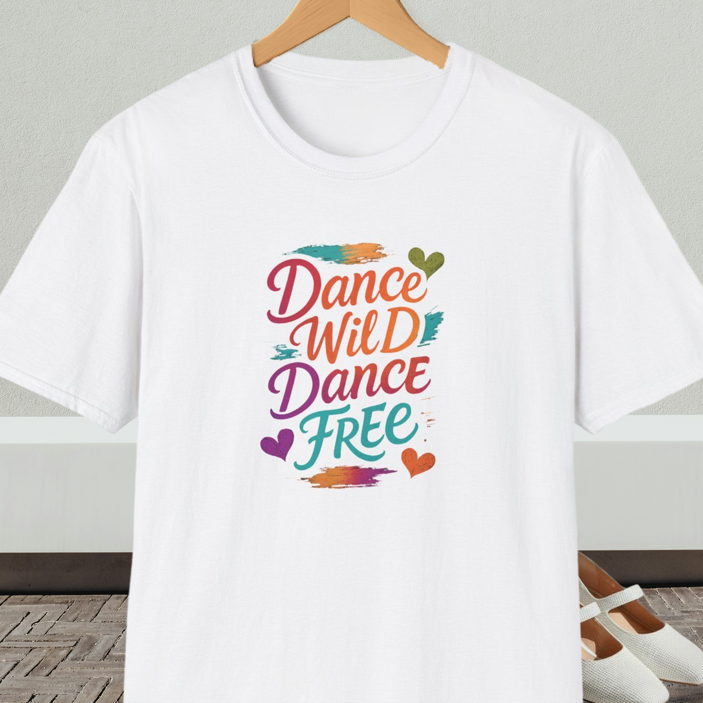 White t-shirt with colorful 'Dance Wild Dance Free' text, on a hanger against a neutral background.
