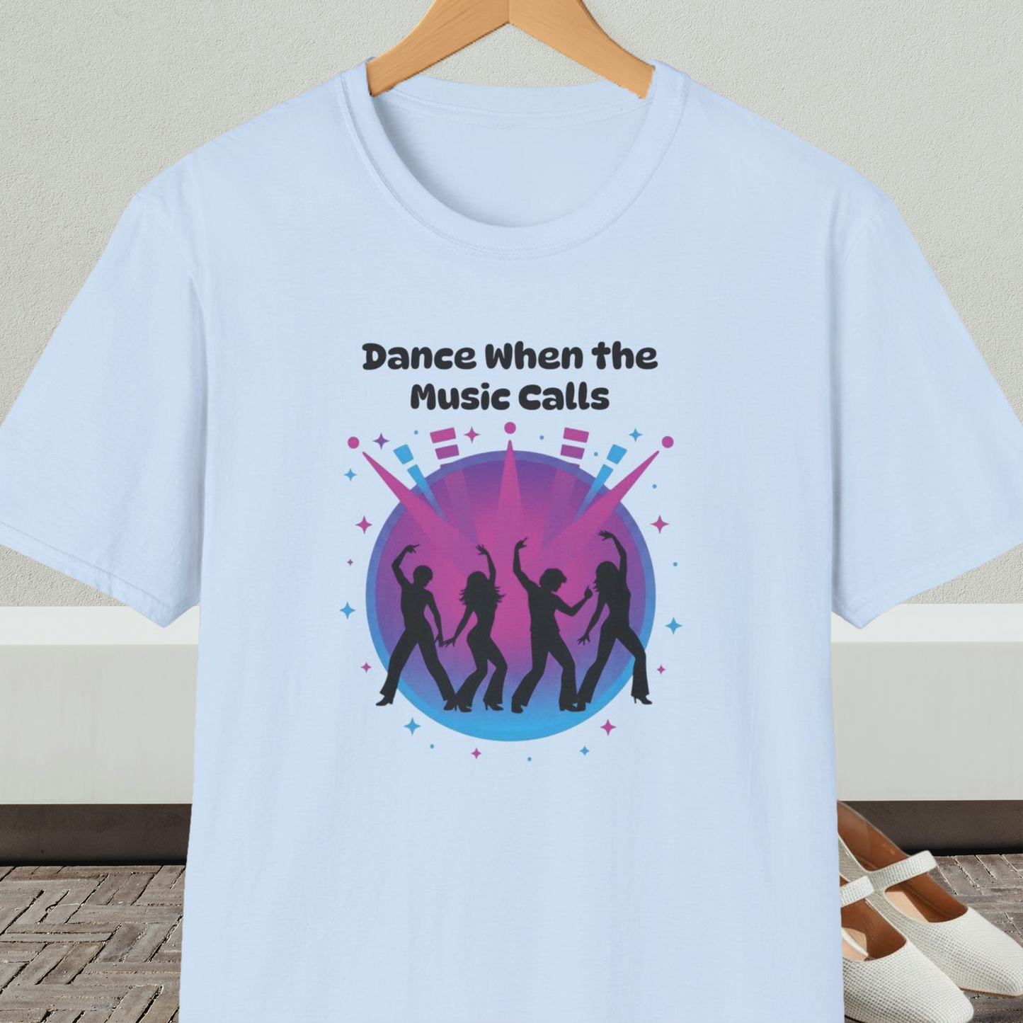 Light blue t-shirt with 'Dance When the Music Calls' dance club design, on a hanger against a neutral background.