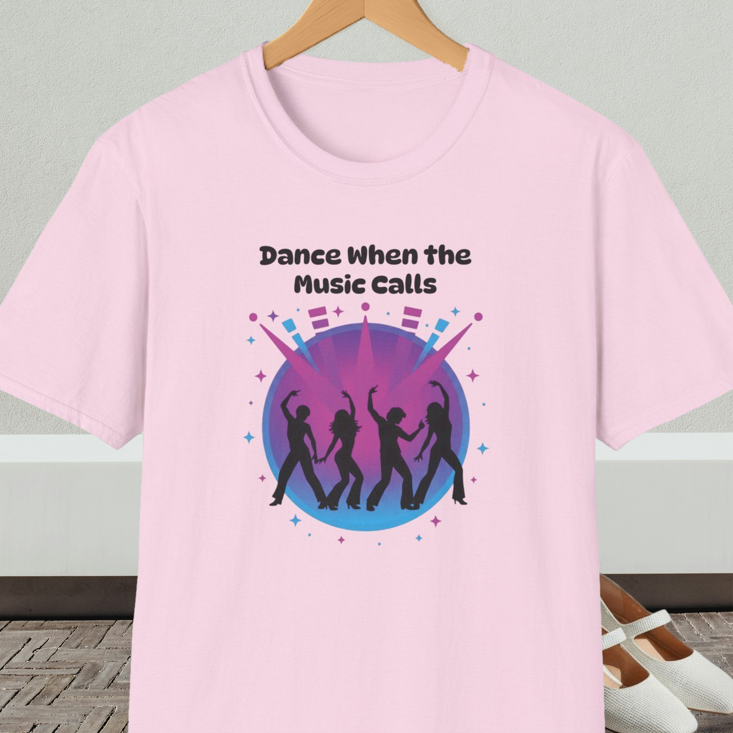 Light pink t-shirt with 'Dance When the Music Calls' dance club design, on a hanger against a neutral background.