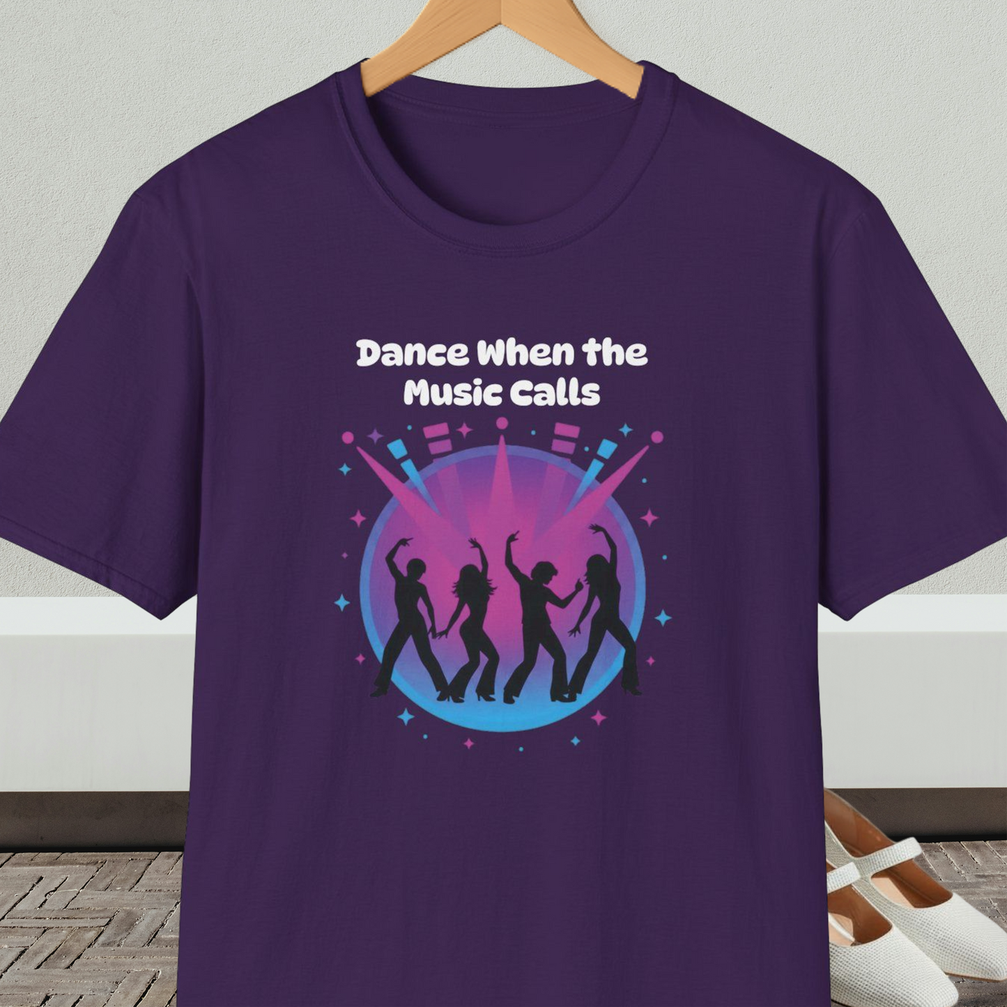 Purple t-shirt with 'Dance When the Music Calls' dance club design, on a hanger against a neutral background.