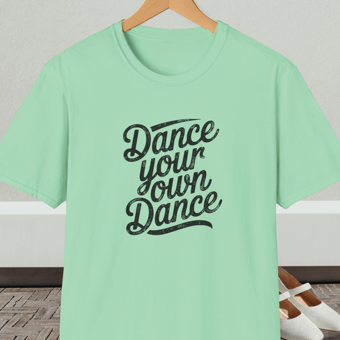 Mint green t-shirt with 'Dance your own Dance' text, on a hanger against a neutral background.