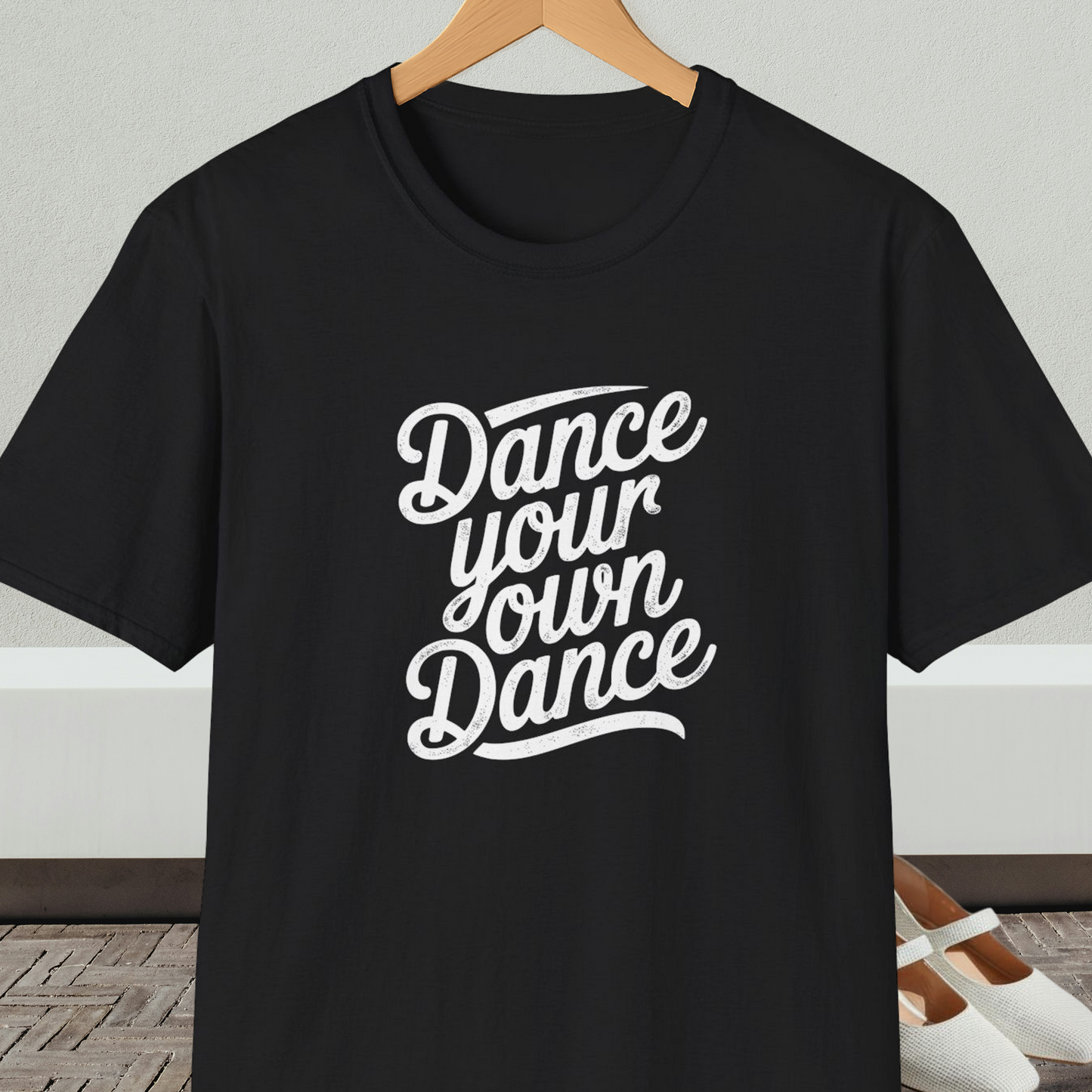 Black t-shirt with 'Dance your own Dance' text, on a hanger against a neutral background