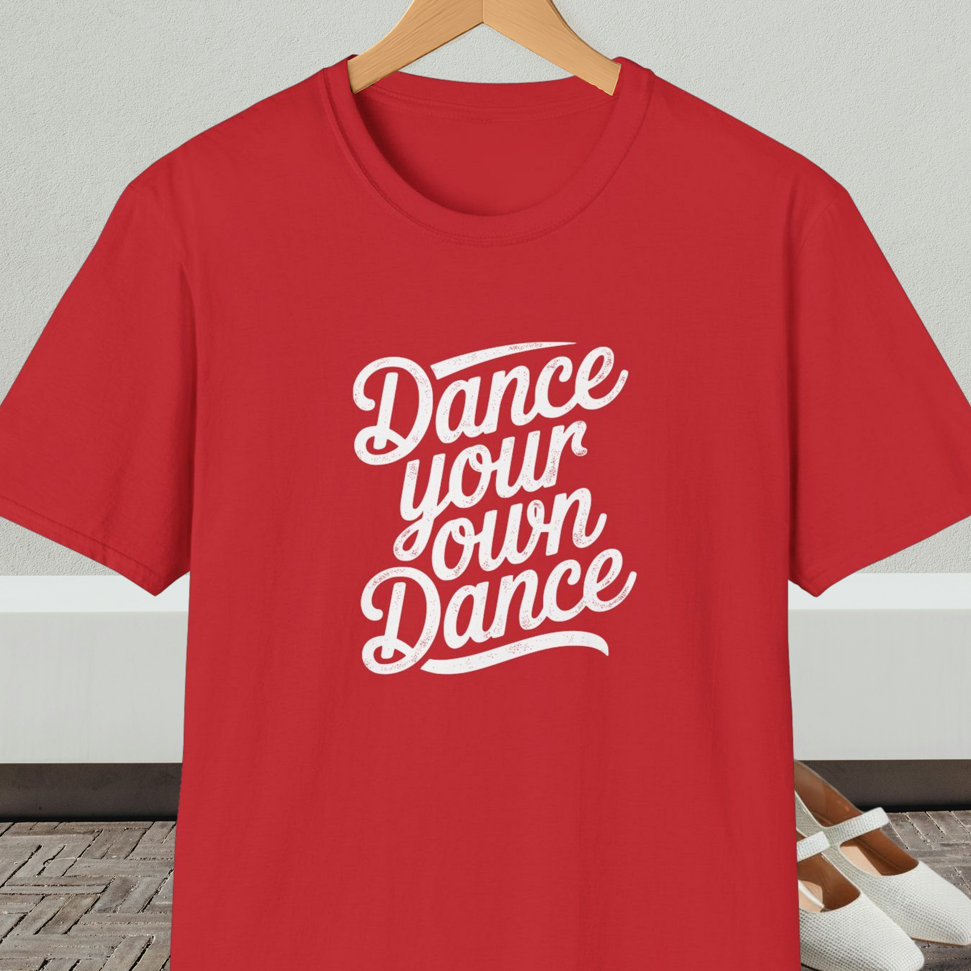 Red t-shirt with 'Dance your own Dance' text, on a hanger against a neutral background