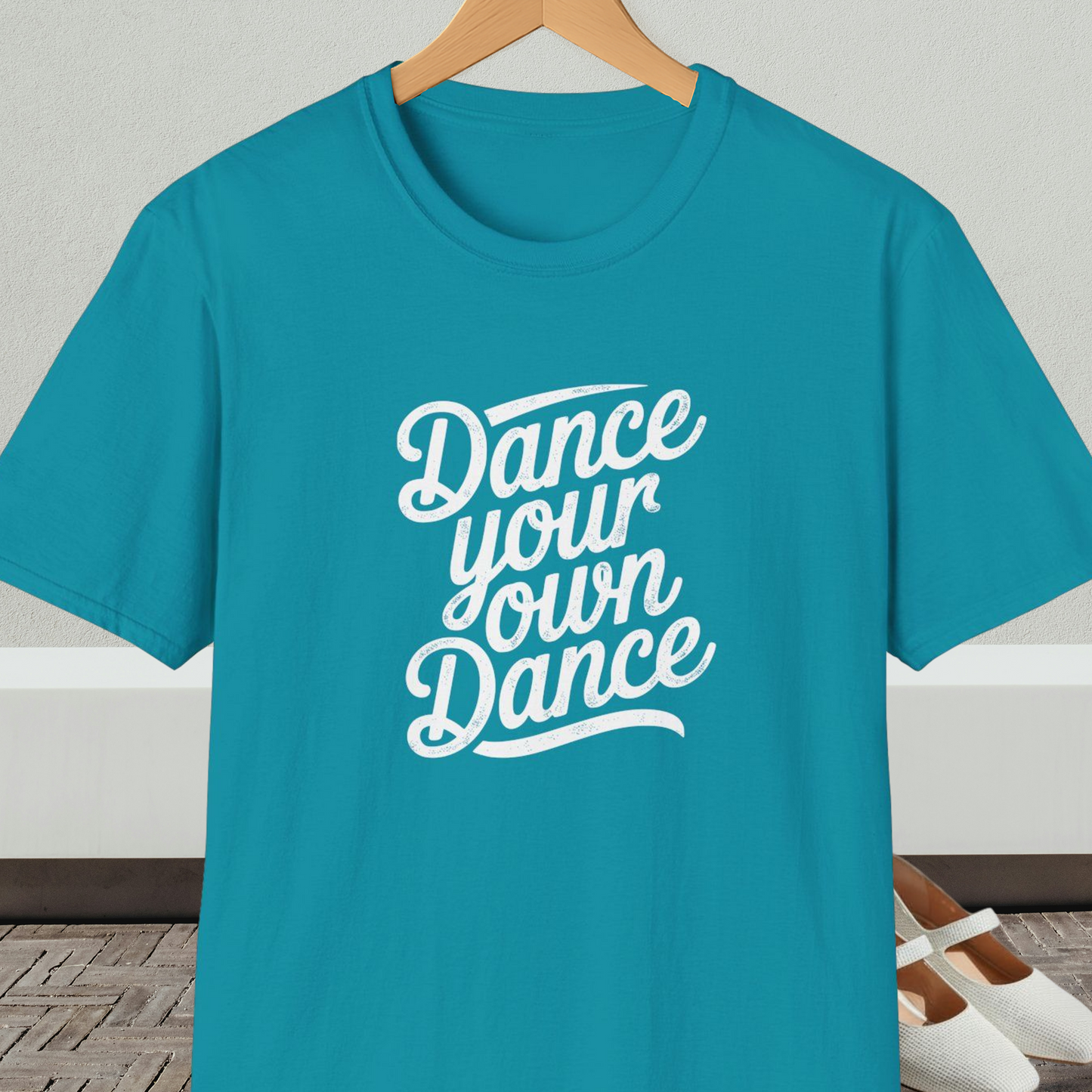 Teal t-shirt with 'Dance your own Dance' text, on a hanger against a neutral background