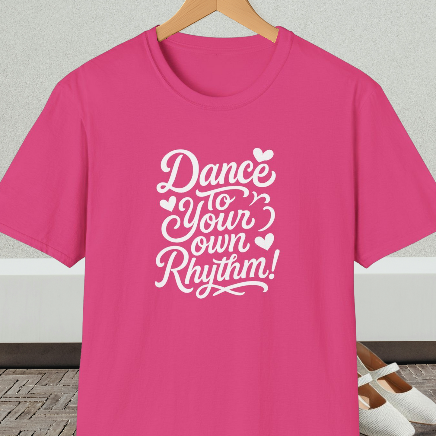 Pink t-shirt with 'Dance to Your Own Rhythm!' text, on a hanger against a neutral background.