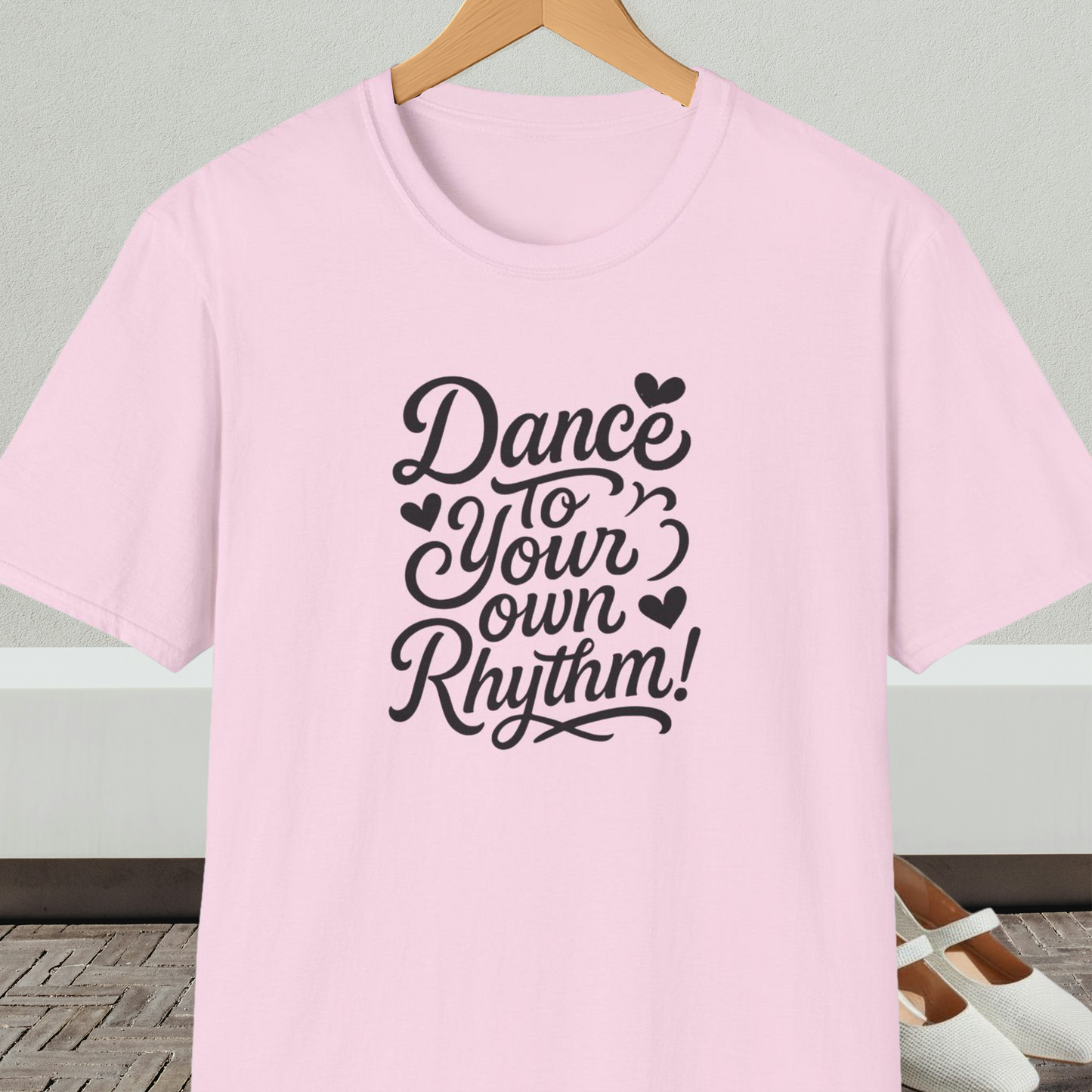 Light pink t-shirt with 'Dance to Your Own Rhythm!' text, on a hanger against a neutral background.