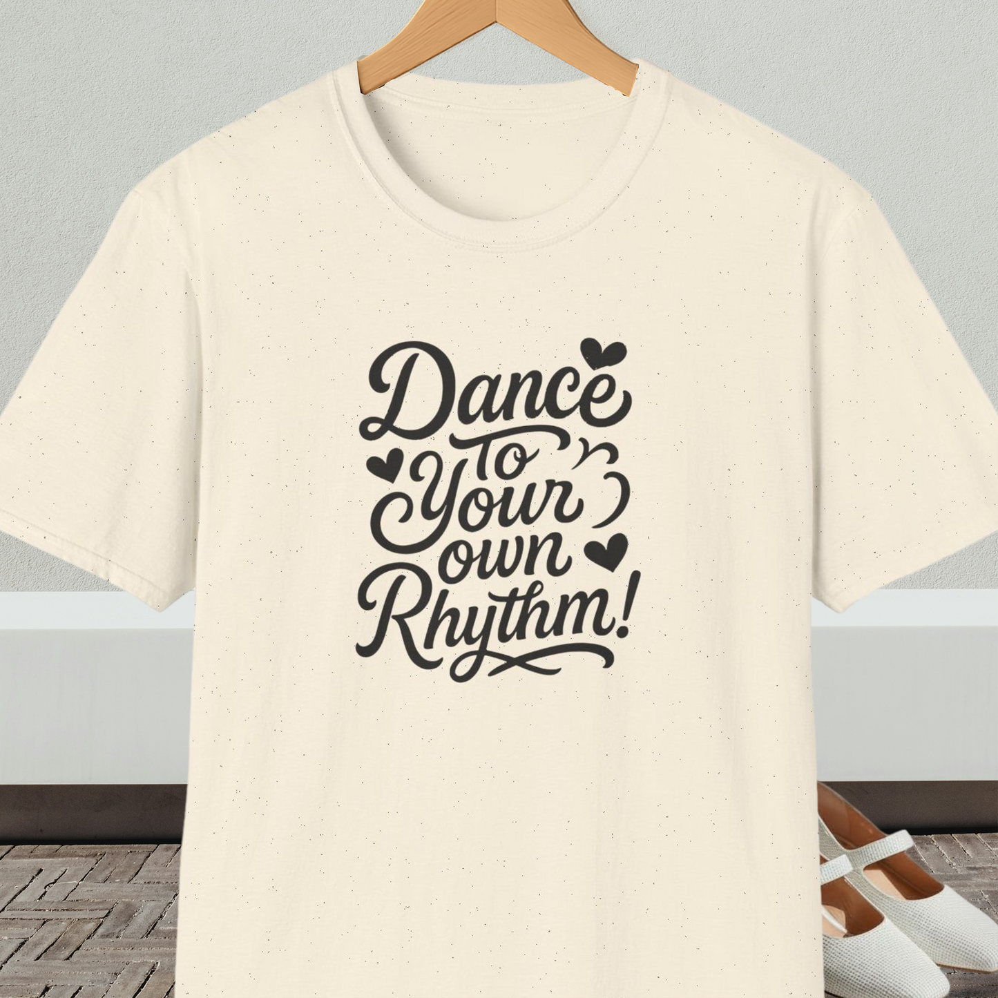 Natural beige t-shirt with 'Dance to Your Own Rhythm!' text, on a hanger against a neutral background.