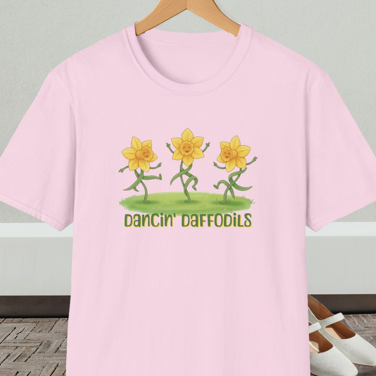 Light pink t-shirt with 'Dancin' Daffodils' design, on a hanger against a neutral background.