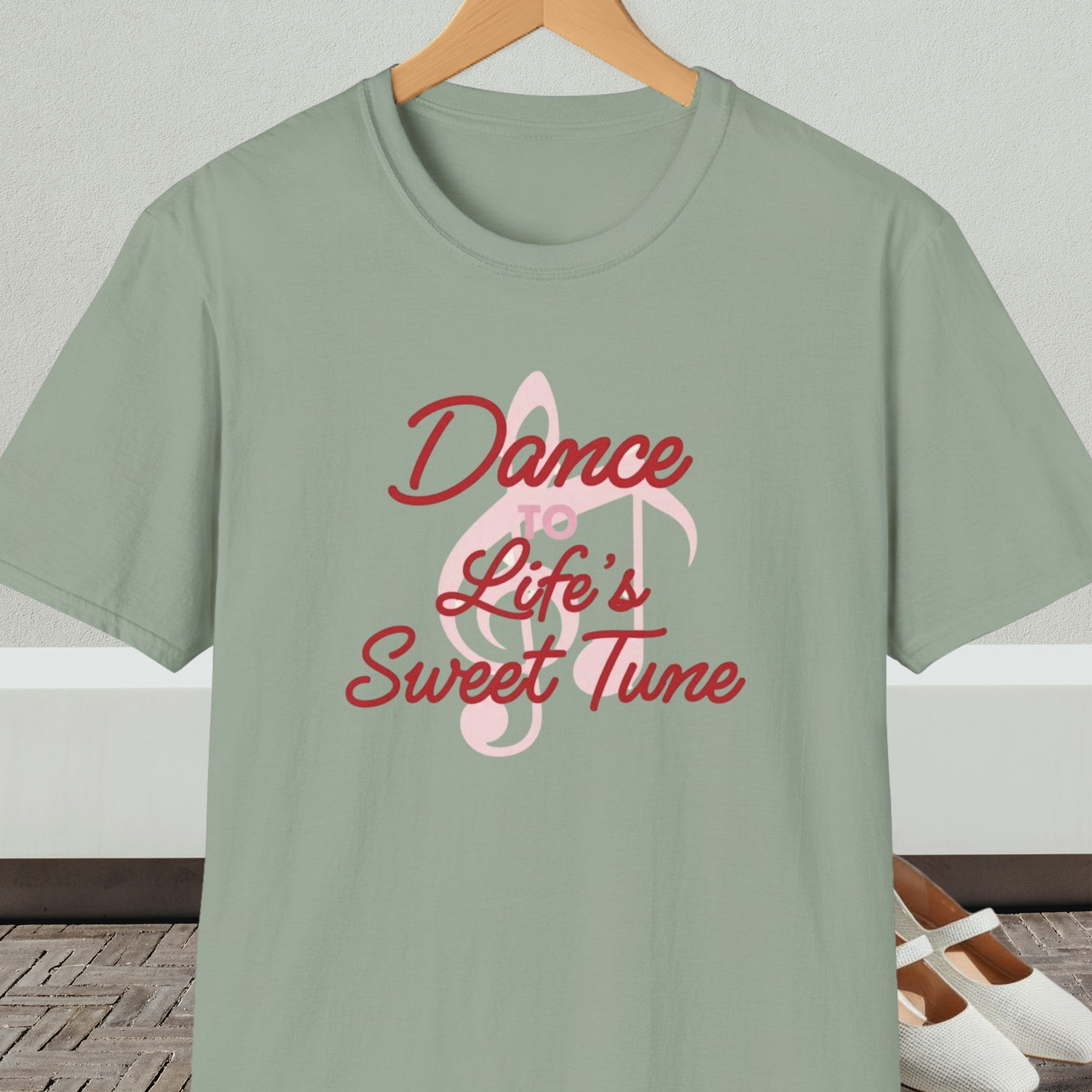 Sage green t-shirt with 'Dance to Life's Sweet Tune' text and pink musical note design, on a hanger against a neutral background.