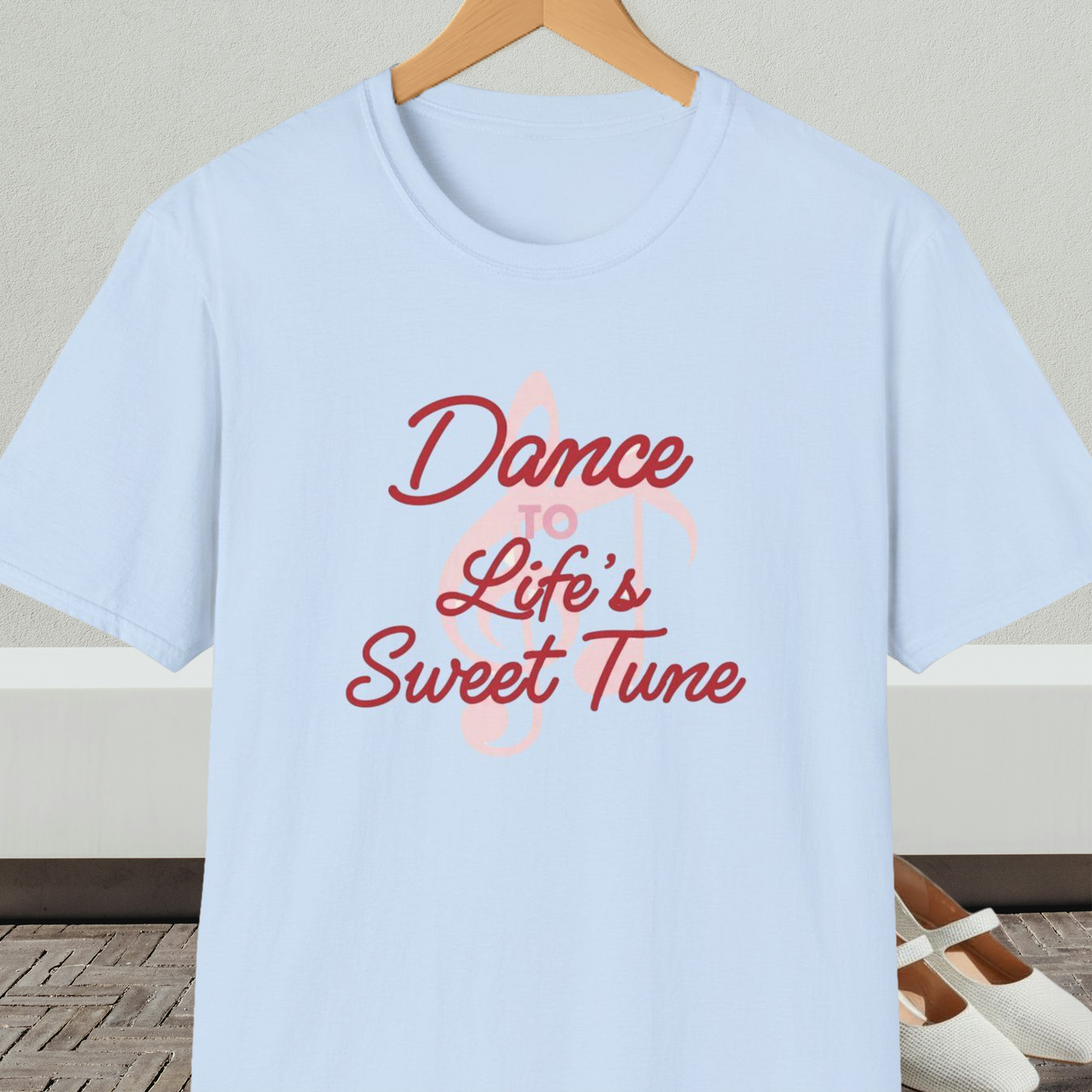 Light blue t-shirt with 'Dance to Life's Sweet Tune' text and pink musical note design, on a hanger against a neutral background.