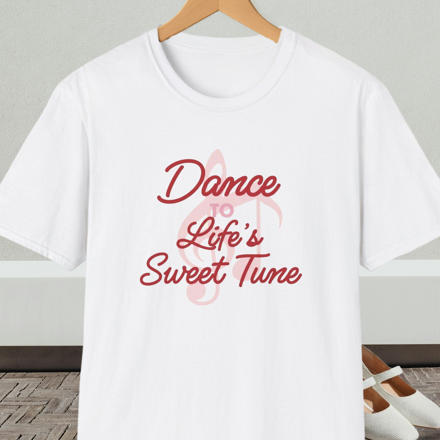 White t-shirt with 'Dance to Life's Sweet Tune' text and pink musical note design, on a hanger against a neutral background.