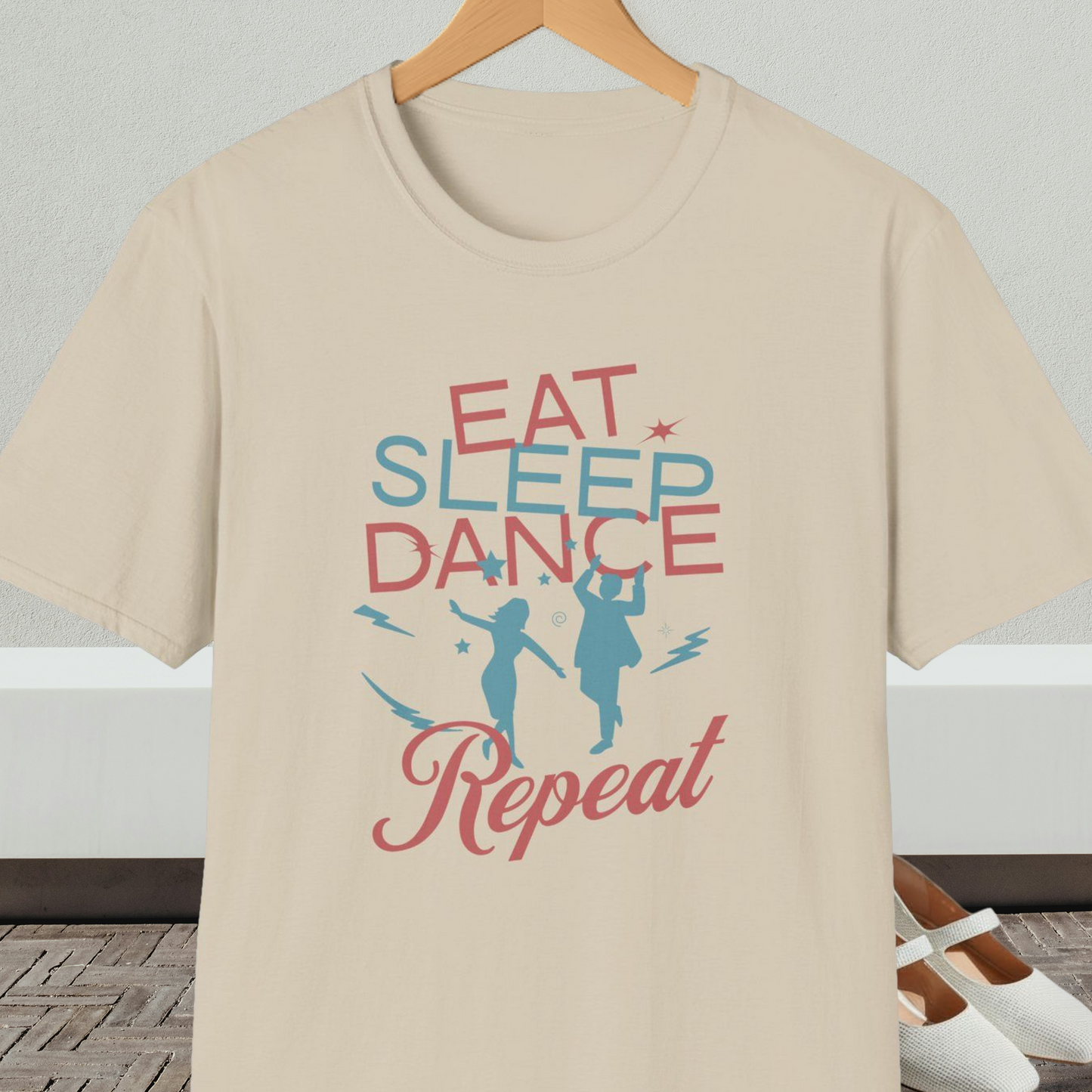 Beige t-shirt with 'Eat Sleep Dance Repeat' text and graphics on a hanger.