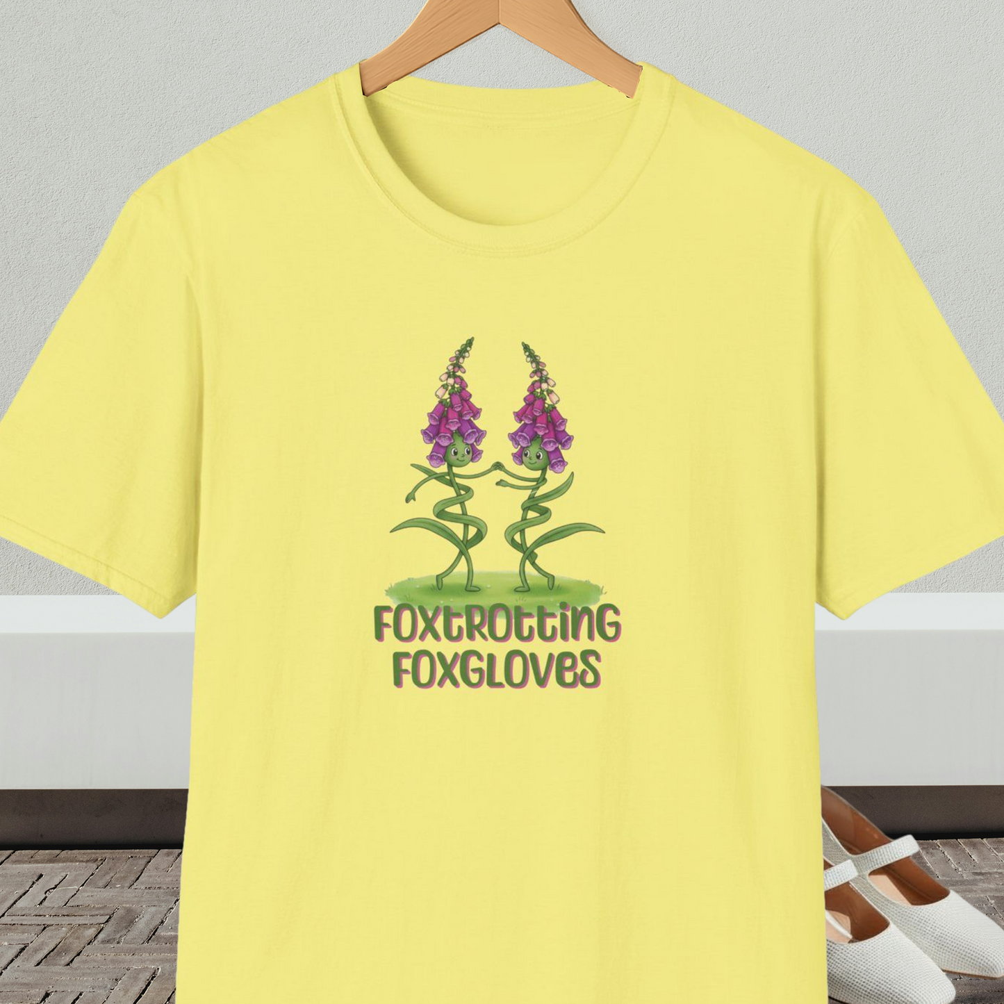 Yellow t-shirt with 'Foxtrotting Foxgloves' design, on a hanger against a neutral background.