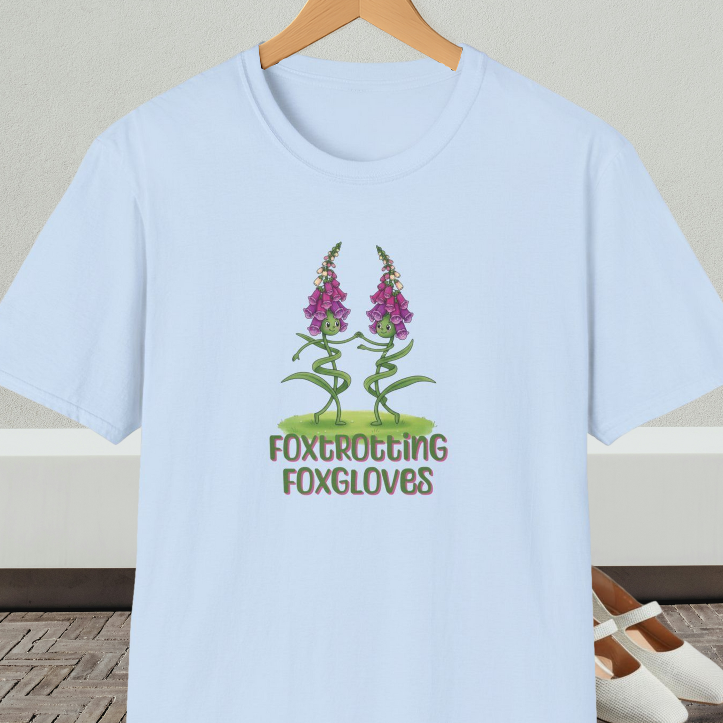 Light blue t-shirt with 'Foxtrotting Foxgloves' design, on a hanger against a neutral background.