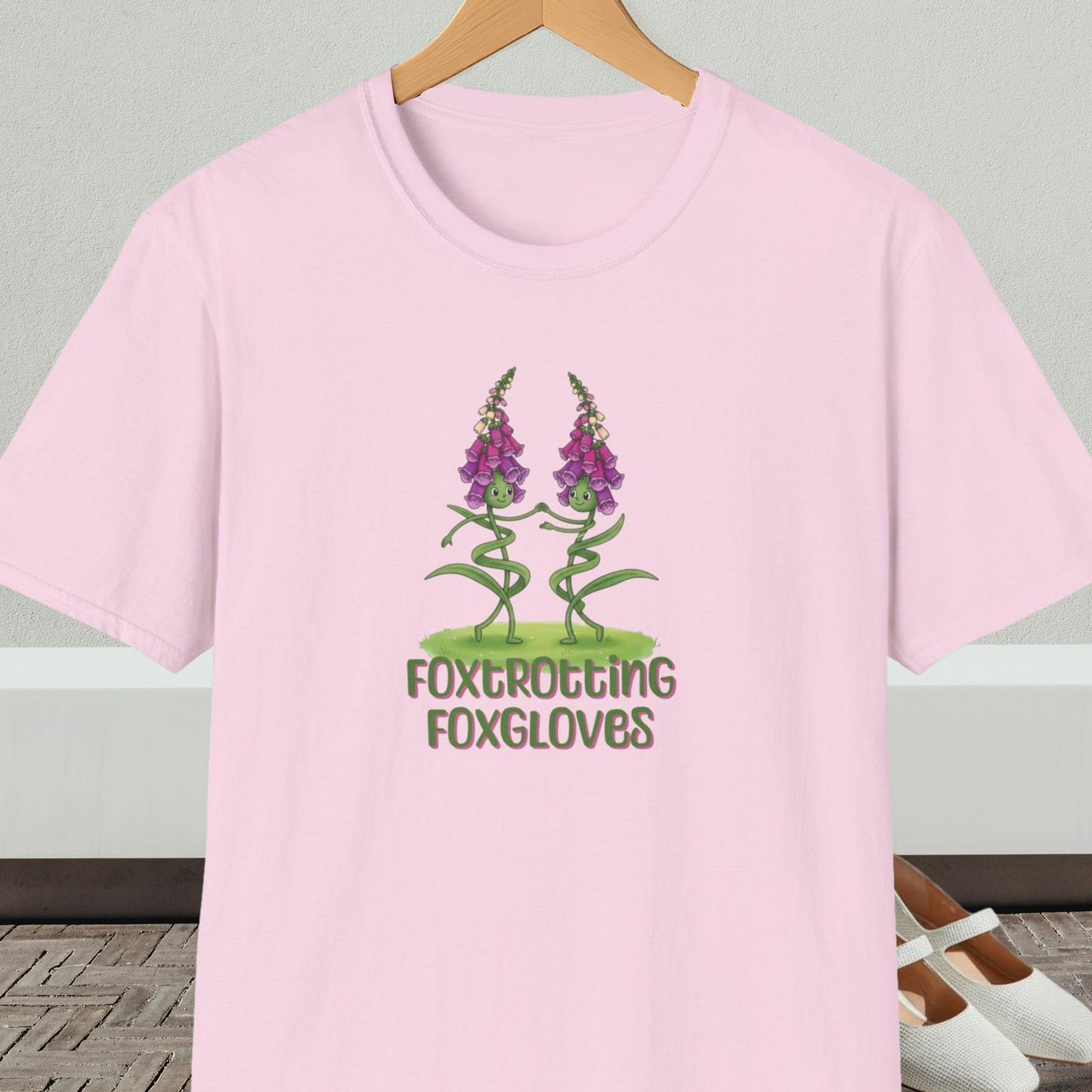 Light pink t-shirt with 'Foxtrotting Foxgloves' design, on a hanger against a neutral background.