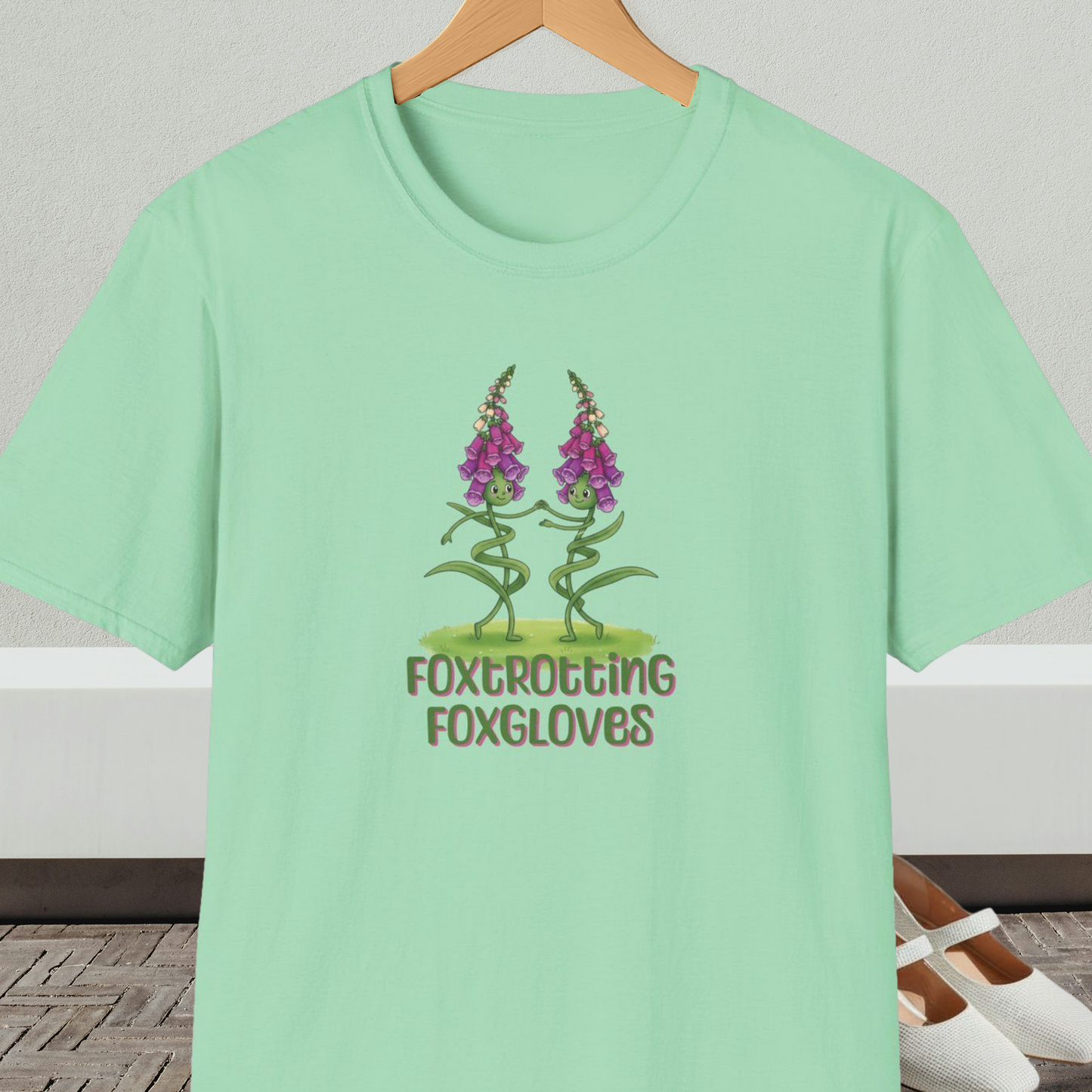 Mint green t-shirt with 'Foxtrotting Foxgloves' design, on a hanger against a neutral background.