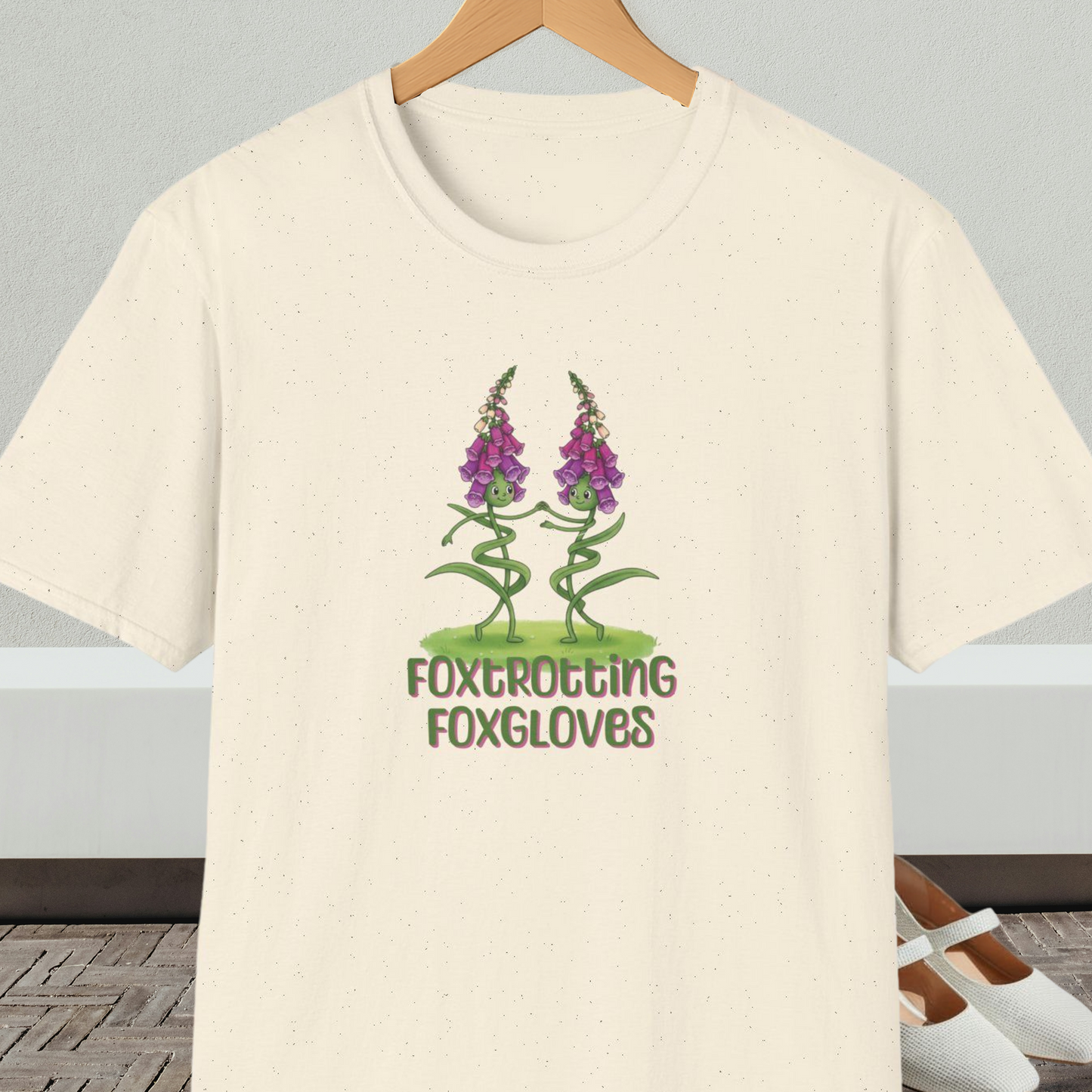 Natural beige t-shirt with 'Foxtrotting Foxgloves' design, on a hanger against a neutral background.