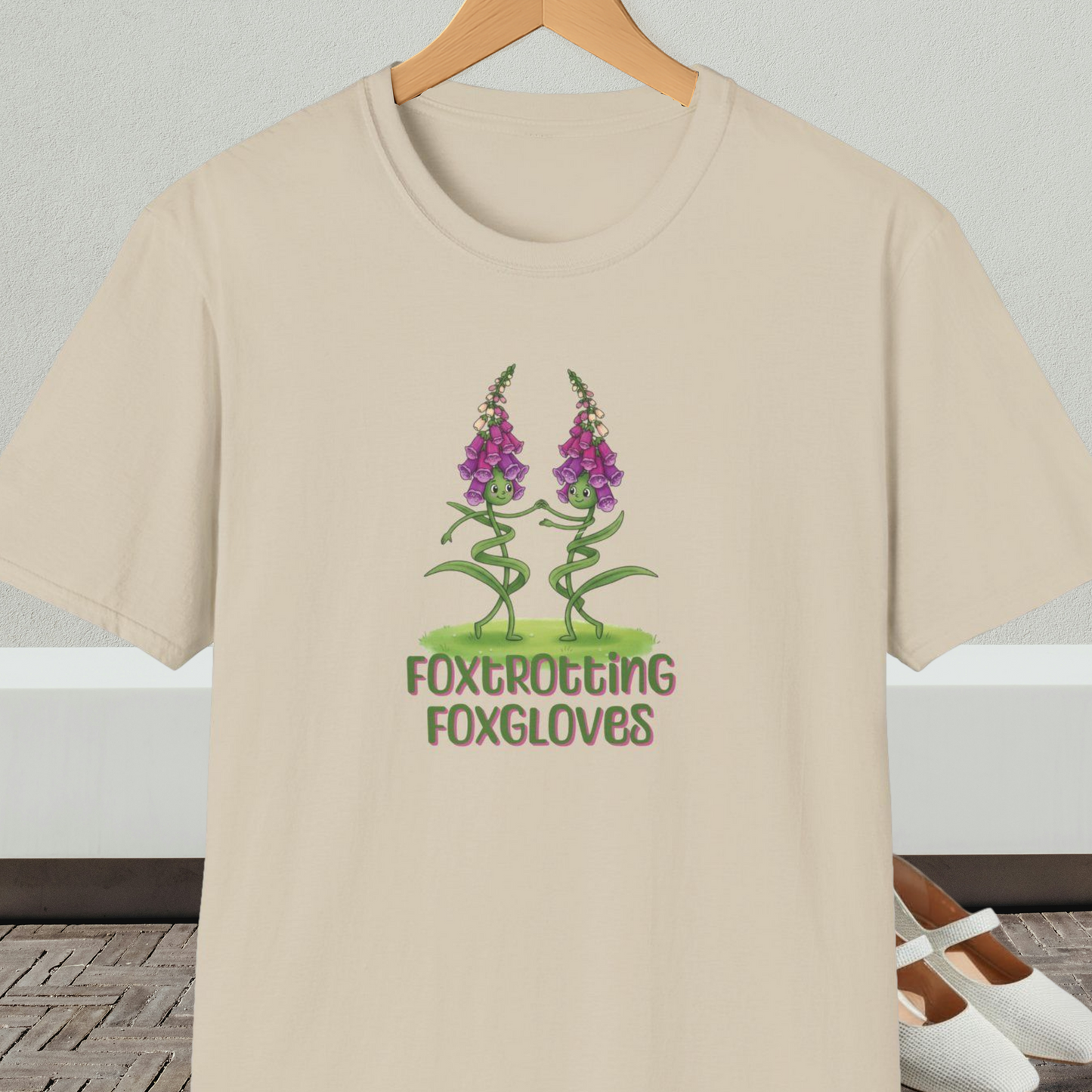 Beige t-shirt with 'Foxtrotting Foxgloves' design, on a hanger against a neutral background.