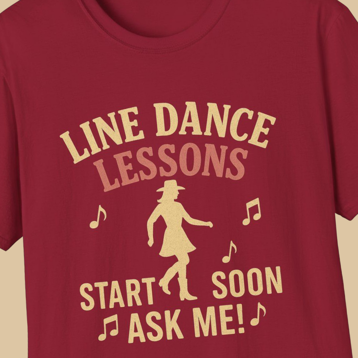A close-up of a red t-shirt featuring a retro-style graphic print in a light tan color. The graphic reads 'LINE DANCE LESSONS START SOON ASK ME!' accompanied by musical notes and a silhouette of a woman in a cowboy hat and dress.